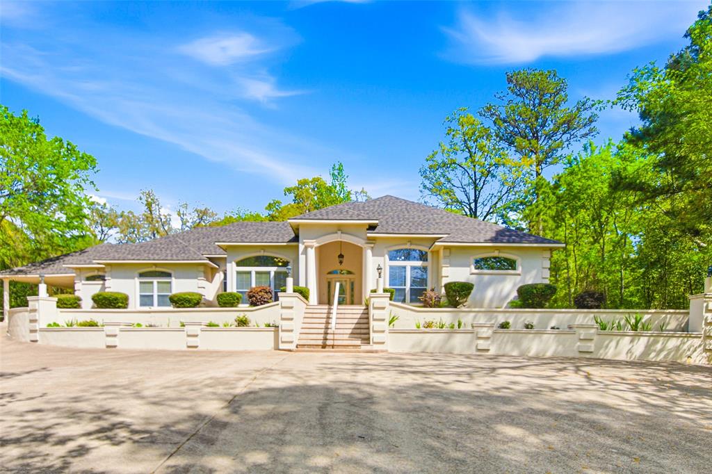 Arrive through a private gated entrance flanked by stucco columns and mature hardwoods to discover this stunning custom Mediterranean-style home nestled on 2.07 wooded acres in Tyler. A sweeping concrete drive leads to the impressive columned facade with arched windows and professional landscaping. Inside, soaring ceilings and an abundance of natural light greet you through an elegant entry door with leaded glass insets and a dramatic arched transom. The spacious great room boasts a curved tray ceiling, wood-burning fireplace with ornate white mantle, and built-in shelving — perfect for relaxing or entertaining. The well-appointed kitchen offers white cabinetry with rope detail, dark granite countertops, center island, tile backsplash, and stainless steel French door refrigerator. The luxurious primary suite includes a spa-like bath with a large walk-in shower with dual shower heads, soaking tub surrounded by mirrors, dual vanities with gold fixtures, and an oversized walk-in closet with abundant natural light. The spacious utility room features cabinetry, tile counters, and washer and dryer connections. Outside, enjoy East Texas living at its finest on the full-length covered back porch with columned veranda, lush lawn, established garden beds, raised vegetable planters, and a separate detached garage and workshop. White board fencing adds classic charm throughout the grounds. Located minutes from Tyler's Loop 49, South Broadway shopping, Brookshire Grocery, UT Health Tyler, and top-rated Whitehouse ISD schools. Easy access to US-69.