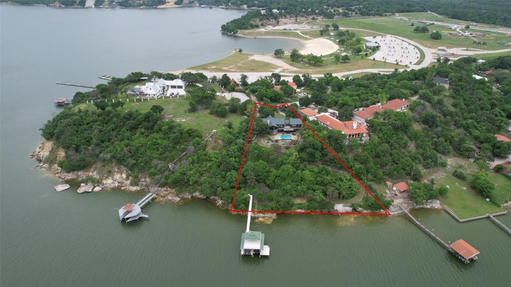 Perched on a scenic bluff just past Twin Points Park, this waterfront retreat offers breathtaking sunset views over Eagle Mountain Lake. Set on approximately 1.2 acres, the home features three bedrooms and two baths upstairs, along with a flexible fourth bedroom or den on the main level. The main living area showcases floor to ceiling windows and a striking stone fireplace, while the spacious kitchen is equipped with an island, double ovens, and beautiful lake views. A secondary living area with a kitchenette provides the perfect setup for guests or a mother-in-law suite. A two car carport plus a circle drive offers ample parking. Outdoor amenities include a pool, second floor balcony, storage shed, private trolley to the water, and an impressive two story dock complete with a boat lift and two personal watercraft lifts, designed for effortless lakefront living.