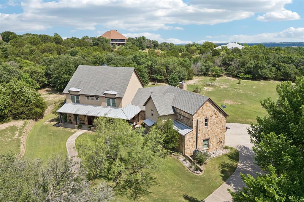 Seeking a peaceful, private retreat with luxury amenities and picturesque Texas countryside views—just 30 minutes from downtown Fort Worth? This exceptional custom estate, situated on 6.5 acres of rolling terrain and mature trees, offers the perfect blend of refined living and rural tranquility.
Showcasing timeless modern farmhouse architecture and outstanding curb appeal, this thoughtfully designed home features rich, high-end finishes throughout, including hand-scraped hardwood floors, coffered ceilings, exposed wood beams, and stunning stone accents.
The luxurious primary suite with expansive windows overlooking the surrounding landscape is a perfect sanctuary.  The spa-inspired primary bath is filled with natural light and complemented by a spacious custom walk-in closet.
Designed for both everyday living and entertaining, the open-concept floorplan seamlessly connects the family room, kitchen, and dining areas. Large gathering spaces flow effortlessly to the screened porch, complete with a stone fireplace, creating the perfect indoor-outdoor entertaining experience.
A private secondary ensuite bedroom is thoughtfully positioned on the opposite side of the home, making it ideal for guests or multigenerational living. Upstairs, you'll find two additional bdrms, a dedicated office or craft room, and a spacious secondary living area.
Outdoor living is impressive, with an expansive covered patio, firepit area, and ample space for recreation, relaxation, and enjoying the natural beauty of the property. Above the oversized 3 car garage, a versatile bonus room provides additional space for hobbies, recreation, or extra living area. 
A separate, fully equipped workshop offers space for woodworking, hobbies, or equipment storage.
Meticulously designed and maintained, this one-of-a-kind property offers a rare opportunity to enjoy luxury country living without sacrificing convenience. A truly exceptional home that must be experienced in person.