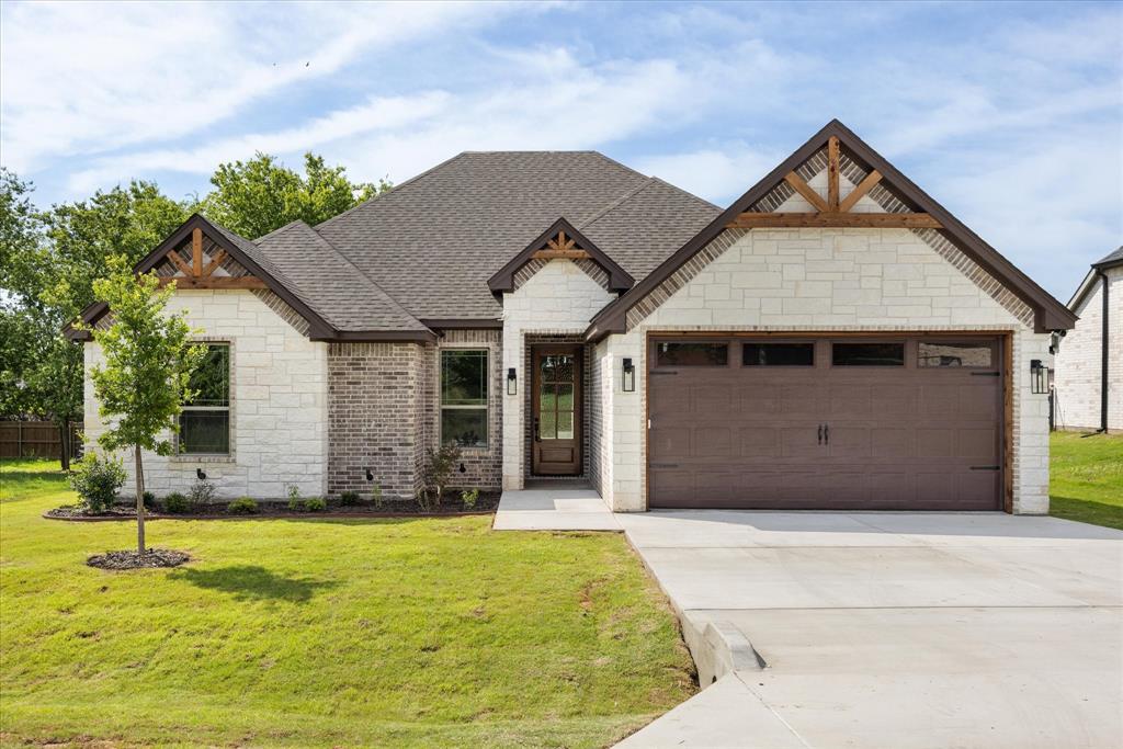 New construction in Canyon Creek built by S&R Homes, featuring a stone and brick exterior with wood accents and an open-concept layout. Inside, you'll find wood-look flooring, a floor-to-ceiling stone fireplace, and a kitchen with quartz countertops, custom cabinets, subway tile backsplash, oversized island, and walk-in pantry. Split-bedroom floorplan with modern finishes throughout and convenient access to Granbury shopping, dining, and lake Granbury.
