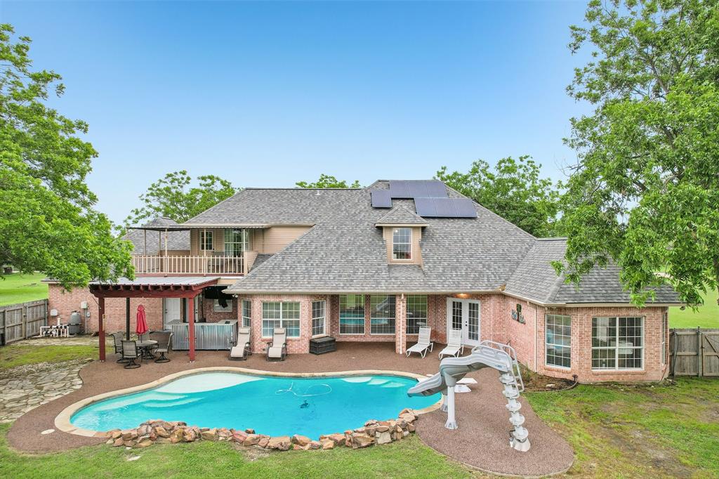 1 acre in Ennis, TX featuring a 5 bedroom, 3.5 bath home with 3,226 sq ft built in 2000, a 24x40 insulated workshop with electricity, 2 car carport, and 3 car garage. Recently upgraded concrete driveway provides additional parking space and convenience. The backyard offers a resort style pool with waterfall and water slide, along with recently added rubber cap surfacing for durability and comfort around the pool and patio, all surrounded by mature pecan trees. Fully paid off solar panels provide long term energy savings. This beautifully maintained home offers a functional open floor plan designed for everyday living and entertaining. A welcoming entry with upgraded rubber cap flooring creates a clean, durable, and modern first impression. As you enter, you find a dedicated office space, an open living room with a brick fireplace, abundant natural light, and large windows overlooking the backyard. The kitchen includes granite countertops and ample cabinetry, with a dining area that flows seamlessly for gatherings. The laundry room includes a sink and storage cabinets. The first floor features a split primary suite for added privacy. One secondary bedroom connects directly to the primary closet, offering flexibility for a nursery, gym, or flex space. A full bathroom serves the secondary bedrooms, along with a half bath with convenient outdoor access to the pool. Upstairs includes a media room with balcony access, an additional bedroom or game room, and a full bathroom, creating a private second level retreat. Major updates include recently completed foundation repair with transferable documentation, two water heaters replaced within the last two years, HVAC system serviced twice yearly across three AC units, and septic system serviced every four months with the seller covering an additional year, and freshly repainted. Located in a quiet neighborhood with a dead end feel and easy access to Highway 287. Everything a Texas home has to offer on a full acre in Ennis.