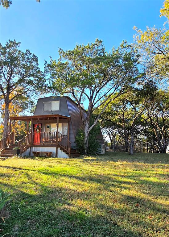 Welcome to your new lake house or investment property! This 2-bedroom, 1.5-bath A-frame sits on just over a quarter-acre, surrounded by mature trees, making it feel like your own private world. Downstairs, you'll find a cozy living room, half bath, and remodeled eat-in kitchen. Upstairs are 2 bedrooms with large closets and a full bath. Has a newer metal roof and AC unit. The backyard is the heart of this property, offering views of Lake Granbury, a fire pit, and plenty of space to entertain. There's a private outdoor shower for post-lake activities or washing pets. The utility room offers extra storage. Currently used as an STR, the home rents for an average of $200 per night and has a 5 star rating as a super host.  All furniture and decor is negotiable but will leave the fridge, washer and dryer. The seller offers up to $5,000 in concessions for rate buy-down or closing costs with an acceptable offer. Note: Indian Harbor is a gated community, requiring a licensed agent for entry.
All information deemed reliable but not guaranteed, buyer and buyers agent to verify.