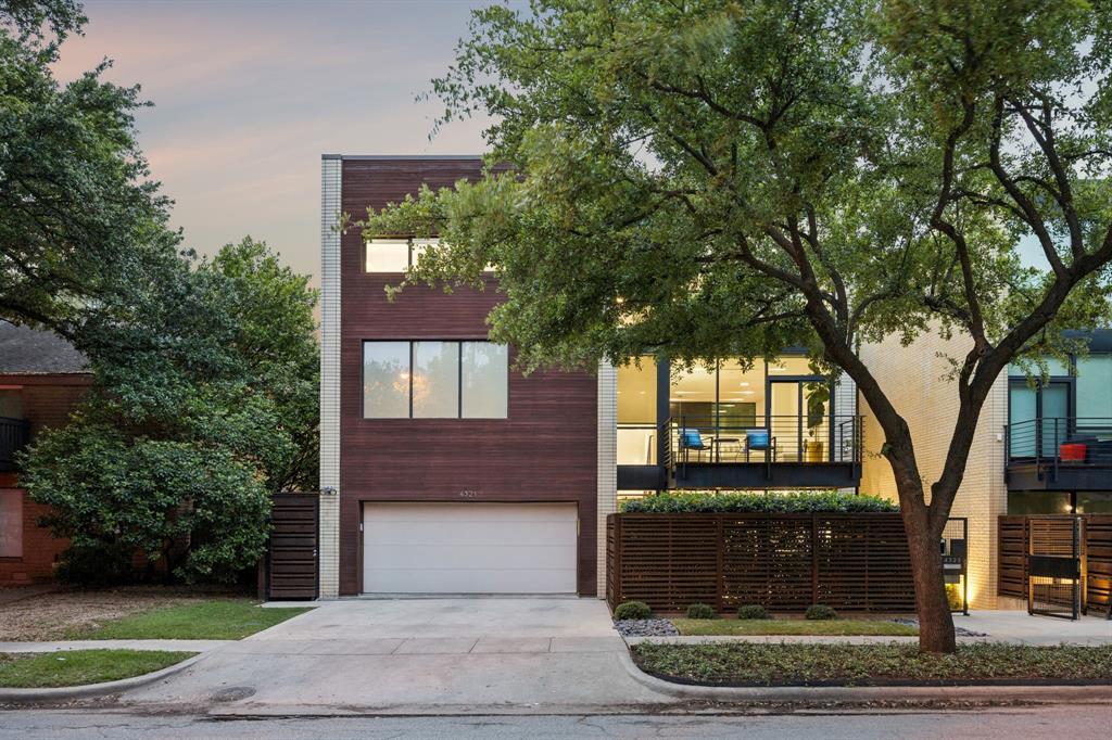 Set within the Travis Walk-Katy Trail district and conceptualized with the art connoisseur in mind, 4321 Travis Street is no ordinary townhome. Across three levels, this residence captures the allure of urban living — design that’s fluent in both comfort & finesse and genuine privacy that places the energy of the city just beyond its doorstep. The exterior is well-considered: taupe masonry, warm wood cladding, floor-to-ceiling windows that glow at dusk. Inside, the double-height main living area sets the tone — exposed brick, a floating steel staircase, hardwood floors, and natural light that moves through the residence with intention. Generously scaled, but not excessive. The kitchen is precise. White flat-front cabinetry ascends to the ceiling, a substantial island anchors the space, and professional-grade appliances bring function & form into the same conversation. The dining room opens directly to a private courtyard with a water feature, fireside seating, and mature trees that offer a quiet departure from the pace of the city.
The second-floor primary suite feels understated yet complete. A private balcony and walnut-paneled dressing room amplify the home’s thoughtful sophistication. A coffee bar with dual refrigerator doors and distinct his-and-her shower areas add pockets of convenience. The third level offers flexibility for all phases of life: a mirrored fitness room, entertainment den, and two additional ensuite bedrooms. The elevator that serves all three levels underscores the home’s ease of use, and a gated motor court delivers peace of mind.