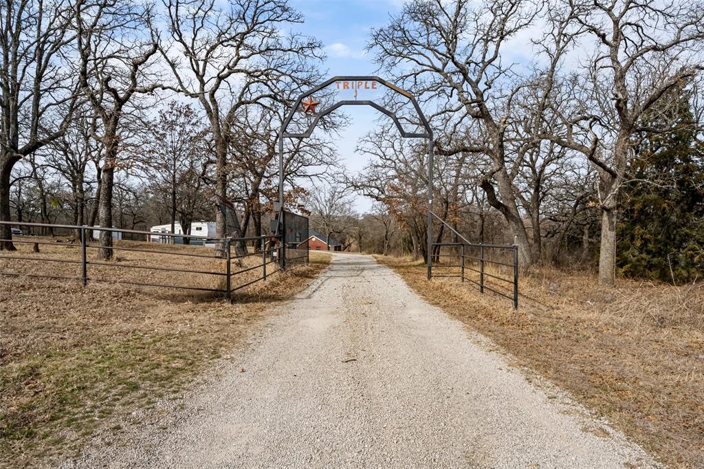Welcome to a beautifully maintained brick home set on six and a half acres in a peaceful rural setting with a blend of open land and mature trees. A custom metal entry arch marks the driveway and creates a welcoming first impression as you arrive home at the TRIPLE J RANCH. This home includes a spacious covered patio that looks out across the acreage and provides an ideal outdoor living space for relaxing, grilling, or gathering with friends and family. Multiple outbuildings add significant utility, including a large foam insulated workshop with tall ceilings, power, and a concrete floor. This building offers excellent space for equipment, projects, storage, or hobby use. A whole house Generac generator provides automatic backup power and adds an extra layer of comfort and reliability.

Inside, the home offers a warm and inviting layout with a brick fireplace in the living area, generous natural light, and an open flow into the dining space and kitchen. The kitchen includes stainless appliances, abundant cabinet storage, and a bright workspace with views of the property. The home provides three bedrooms and two and a half baths, along with a two car garage and an additional three car metal carport that offers excellent covered parking for vehicles, trailers, or equipment. The primary suite includes a double sink vanity and convenient access to the main living areas.

The land includes a wet weather creek along the back boundary and offers room for livestock, recreation, gardening, or future improvements. The acreage provides privacy while still offering convenient access to FM 920 and nearby communities. This property combines comfortable living with practical features and a versatile layout that fits a wide range of needs. Located in Poolville ISD. The home is just north of the intersection of Hwy 199 and 920, where there is a great gas station and convenience store with a good restaurant!! What more could you ask for??