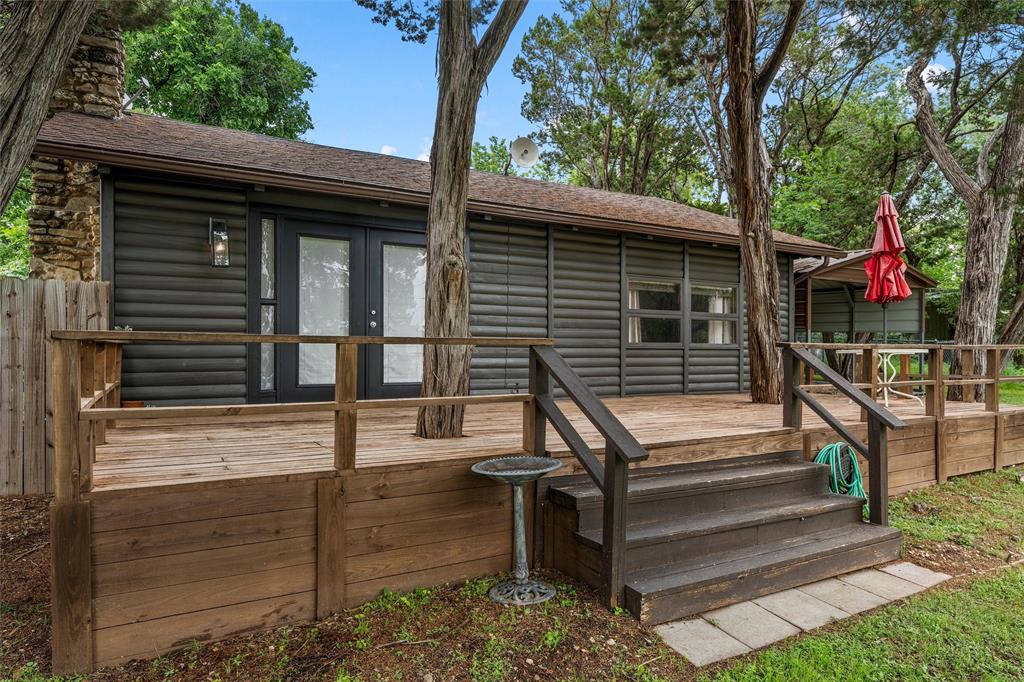 Tucked away with peaceful views of Lake Whitney, this storybook log cabin feels like something straight out of a Ralph Lauren retreat. Blending rustic charm with elevated, designer-inspired finishes, 188 Linda Lee Loop offers the perfect escape—whether you're looking for a weekend getaway, a writer’s haven, or a cozy place to unwind. Renovated in 2021, this 2-bedroom, 1-bath cabin is warm, inviting, and thoughtfully styled throughout. Inside, you’ll find porcelain wood-look tile flooring, a chic kitchen complete with a farmhouse sink and island, and a full-sized stacked washer and dryer for convenience. The wood-burning fireplace anchors the living space, creating the ideal setting for quiet mornings or relaxing evenings. Step outside to a spacious front deck where you can take in serene lake views, or retreat to the private backyard featuring a covered entertaining area—perfect for gathering with friends or enjoying the outdoors in comfort. Additional features include a metal storage building with an attached carport, offering both practicality and extra space. Full of character, style, and charm, this one-of-a-kind cabin captures the essence of lakeside living with a refined, cozy twist.
