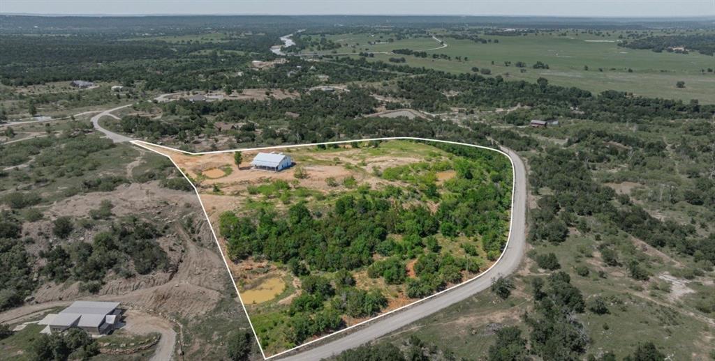 Experience unmatched privacy, panoramic views, and endless possibilities on this stunning acreage property in the highly sought-after gated community of Capstone Ridge on the Brazos. Perched on an elevated homesite, this property offers sweeping views for miles—perfect for enjoying peaceful sunrises, golden sunsets, and star-filled Texas skies. The centerpiece of the property is a beautifully constructed 3,000 sqft barndominium-style building featuring a spacious covered porch, ideal for relaxing or entertaining while taking in the surrounding landscape. Whether you choose to finish out the existing structure into your dream home or utilize it as a shop while building your custom residence, the opportunity here is limitless. The land itself is thoughtfully improved with multiple ponds, mature trees, and a mix of open space and natural terrain—perfect for horses, recreation, or simply enjoying the outdoors. With ample room to expand, this property is well-suited for a private ranch, weekend getaway, or full-time residence. Additional improvements include a septic system, underground electric with 400-amp service, city water already run to the property, water filtration and softener system, 3 ponds on the property , and an RV hookup—perfect for guests or temporary living while you complete the build. Located within a gated community, residents enjoy access to two common areas with direct access to the Brazos River and a private boat ramp for small watercraft—adding even more value and lifestyle appeal. Utilities are already in place, making this property ready for your vision. Whether you’re looking to build, invest, or create your own Texas retreat, this is a rare opportunity to own a premier piece of land with views that truly set it apart. You can now see the Weatherford Firework Show from the property!