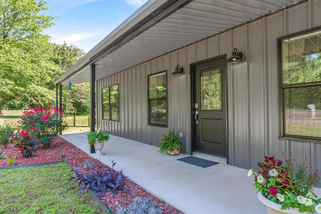 Beautifully maintained and exceptionally clean barndominium situated on approximately 1.79 acres with a large pond, scenic garden area, and peaceful country setting. This energy-efficient 3-bedroom, 2-bath home built in 2024 features an inviting open floor plan with a convenient kitchen, breakfast bar, dining area, and spacious living area filled with natural light. The home also offers a nice-sized laundry area along with large covered front and back porches, perfect for relaxing and enjoying the surrounding views. Additional features include both co-op water and a well, a concrete storm cellar for added peace of mind, and an additional garage-carport with storage providing ample space for vehicles, equipment, or hobbies. With easy access and a beautifully cared-for setting, this property offers the perfect blend of comfort, functionality, and country charm.