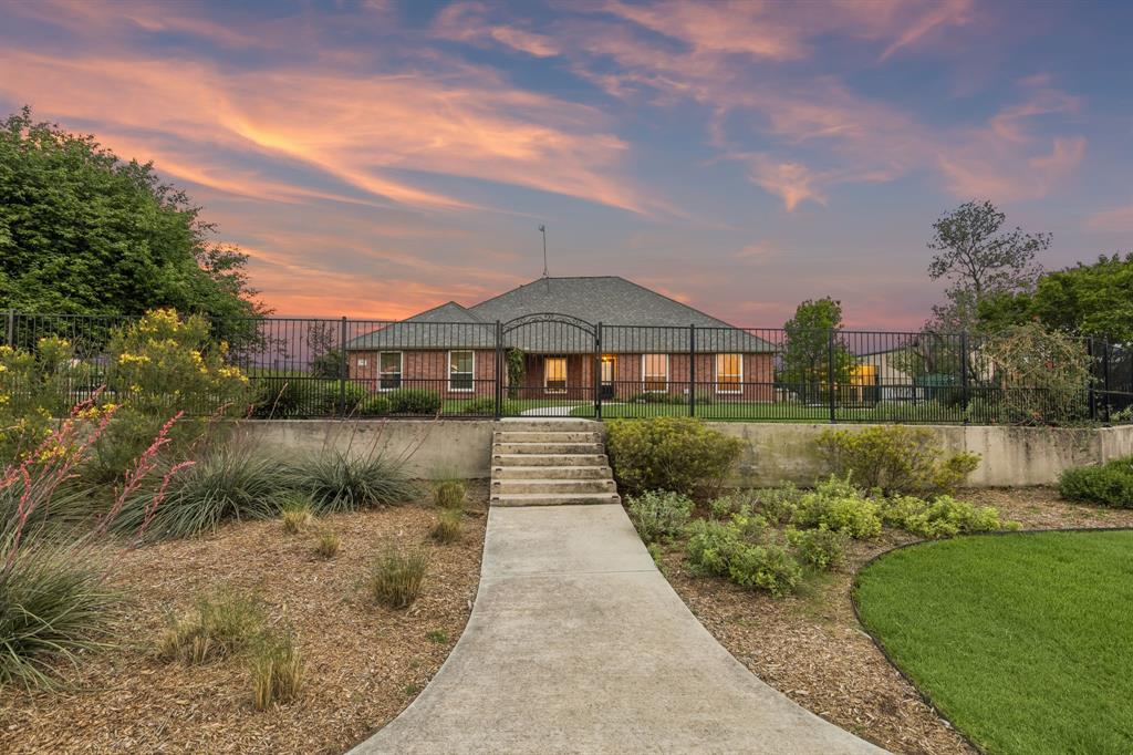 Perfectly situated on over one acre corner lot in the highly sought after community of Sun Valley Estates, this meticulously maintained property has it all. A stunning, elevated homesite framed by extensive manicured landscaping & a classic wrought iron fence. The expansive green space, gardens, & serene sunset views offer the perfect backdrop for outdoor living and show pride of ownership. Main home features 3 generously sized bedrooms, a lovely secondary bath & wonderful storage. The Spacious primary suite features warm wood flooring, vaulted ceilings, & abundant natural light. Spa-inspired primary bathroom featuring dual vanities, a relaxing jetted soaking tub, glass-enclosed shower, & oversized walk-in closet. Beautifully updated kitchen showcases custom-painted cabinetry, rich granite countertops, and a modern mosaic backsplash. The thoughtfully designed layout offers a center island, abundant storage, and seamless connectivity to the main living space—perfect for both everyday living and effortless entertaining. The living room is anchored by a warm brick fireplace and expansive windows that fill the room with natural light. The open-concept design flows effortlessly into the dining area, while durable tile flooring and neutral tones create a timeless, comfortable setting for both relaxing and entertaining. A secondary living space is a wonderful option for a formal den or home office. Impressive, oversized shop measuring approximately 30x52, offering exceptional space for a workshop, storage, or hobby use. The shop includes a private half bath for added convenience and functionality, a 12-foot door, & two 50 Amp plugs for RV & hot tub. Attached is an expansive covered patio overhang, creating the perfect setup for outdoor workspace, equipment coverage, or shaded entertaining. This property offers ideal country living while still having easy access to shopping, dining, & entertainment. Zoned to Award Winning Northwest ISD Schools this home is truly a must see.