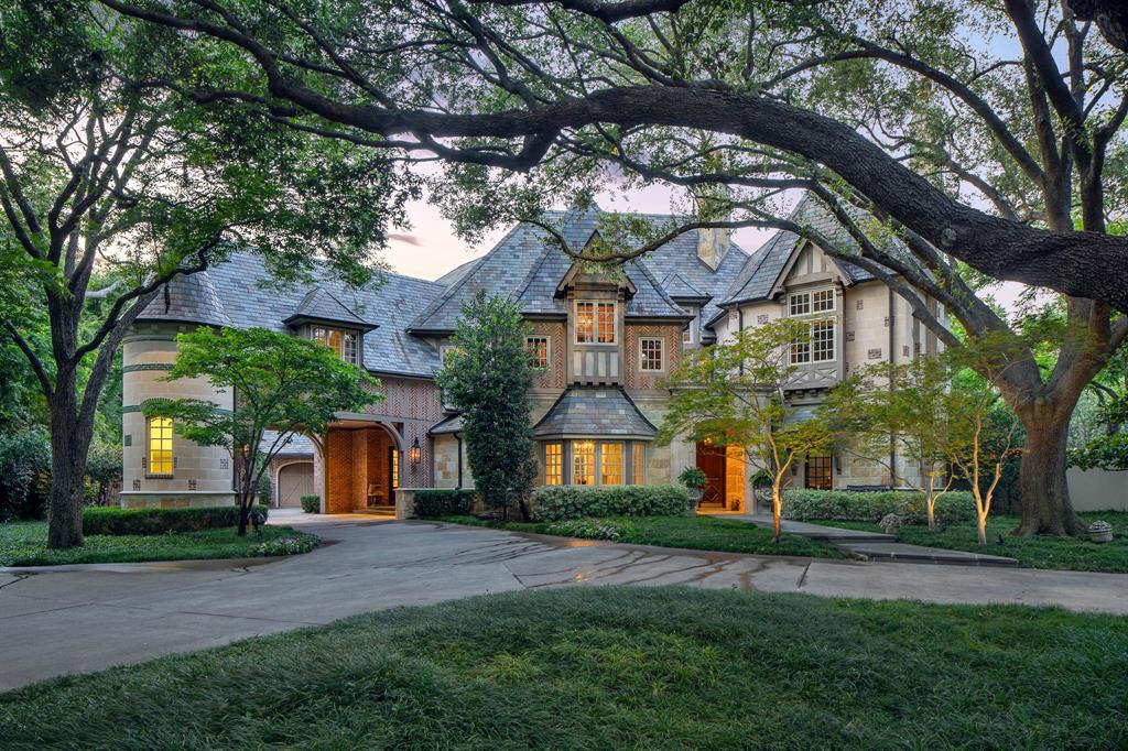 Designed by Richard Drummond Davis and built by Randy Hughes, 5431 Edlen Drive draws from the language of the French countryside — its steeply pitched slate roof, limestone details, and herringbone floors reminiscent of a château shaped by generations. The owners and architect selected the materials themselves during their many trips to France together. The arrival follows through on that particular significance: a gated circular drive canopied by mature Magnolia trees, a stone-clad front door, and porte-cochère with a discreet entry. Inside, the scale is generous. The family room opens wide, a breakfast nook complements the formal dining room, and the music room — an octagonal bay wrapped in windows — revives the kind of dinner party that ends with someone at the piano. The kitchen anchors daily life with a stainless steel island, exposed beams, custom vent hood, and dedicated wine storage. The old world-inspired library serves as the home’s most distinguished focal point. Two stories of hand-crafted millwork draw the eye upward to the chandelier, with shelves climbing to a mezzanine accessible only by an iron spiral staircase. This is the moment the house reveals its full ambition. Upstairs, find a primary suite with a private balcony, his-and-hers closets and lavatories, and three generously sized en-suite bedrooms. The playroom, media room, and balcony round out the second level. A fourth bedroom suite sits on the main floor for added convenience. Four fireplaces warm the rooms that matter most: the family room, library, primary suite, and pool house. Set on a full acre corner lot, the pool house with its own powder room and wet bar ensures afternoons by the pool remain outside. A whole-house generator means the lights stay on, no matter the season. Positioned in Preston Hollow and only minutes from Preston Center, NorthPark, and the energy of the Park Cities, 5431 Edlen Drive was built to last.