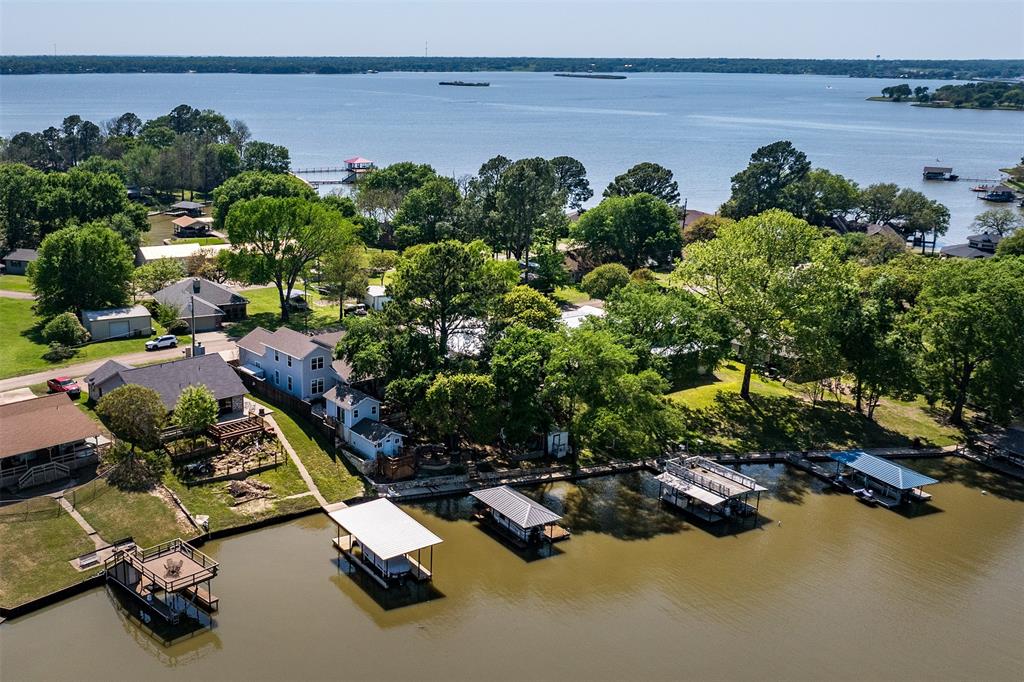 Custom built in 2020, this beautifully designed four-bedroom, three-bath home offers the perfect blend of comfort and lakeside living. The open-concept living and dining area features luxury vinyl flooring, a cozy fireplace, and a dramatic wall of windows that fills the space with natural light and showcases tranquil lake views. The stunning kitchen is equipped with granite countertops, a decorative tile backsplash, stainless appliances, and a spacious island with seating- ideal for gathering with family and friends. The private primary suite is conveniently located on the main level and overlooks the water, offering double vanities and a large walk-in tile shower. Three additional bedrooms and two full baths provide plenty of space for guests. Outdoor living is just as impressive, with lush landscaping, a wonderful covered porch, greenhouse, and a lakeside patio perfect for entertaining. A boathouse with a personal watercraft lift makes enjoying the water effortless. The finished summer room offers flexible space for kids, hobbies, or a peaceful retreat. Additional highlights include an oversized two-car garage, extra parking, and even a private pickleball court- creating a true lakeside lifestyle experience.