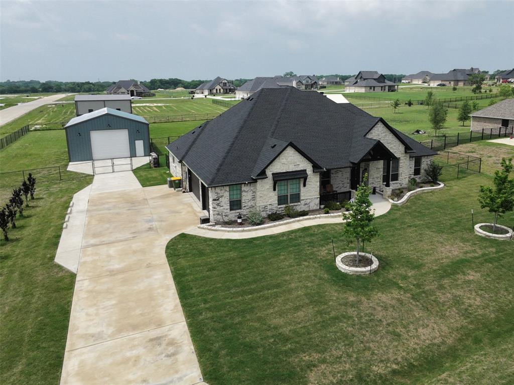 If you are looking to live OUTSIDE THE CITY LIMITS in a spacious, almost new, 1-owner country home offering WONDERFUL curb appeal along with a 1,200sf insulated workshop boasting 14ft walls and 12ft powered Overhead doors on a 1-acre fenced and cross-fenced lot, you have come to the right place! Approaching the home, notice the beautiful brick and rock work as well as the fantastic wood accents. Observe the meticulous design and care that has been given to the gardening beds bordering the home's facade complete with a relaxing covered porch. Enter to find the office conveniently located to your left through the French Doors. The entry hall opens to an expansive open floorplan connecting the living room, dining room, and kitchen all with lofty ten foot ceilings. A charming WBFP is located opposite the entry hall and overlooks the living area. The kitchen exhibits class with walls of floor to ceiling solid wood custom cabinetry accompanied by undermount lighting and hidden built-in spice racks, granite countertops, ss appliances, walk-in pantry, and 9ft island. The master bedroom offers a great view of the backyard and space for a sitting area. The ensuite bath is massive with a large garden tub and separate shower, dual vanities with a make up prep area and more than 15 feet of counter space.  The home can be set up as a 4 bedroom with an office or a 3 bedroom with a 2nd family room and an office as it is currently. The 4th bedroom is 16 x 15 and has ensuite half bath that has private entrance to the backyard and its covered patio making it perfect if you would like to add a pool! The oversized attached garage is approximately 720sf with a depth of 24ft and raised 8ft garage doors to accommodate large vehicles.  New 30-year roof installed in 2025; high-speed fiber optic cable service; security cameras and security system stay with the home; 2in faux wood blinds throughout; decorative lighting; mudroom just off garage; desirable Maypearl ISD…well worth visiting!