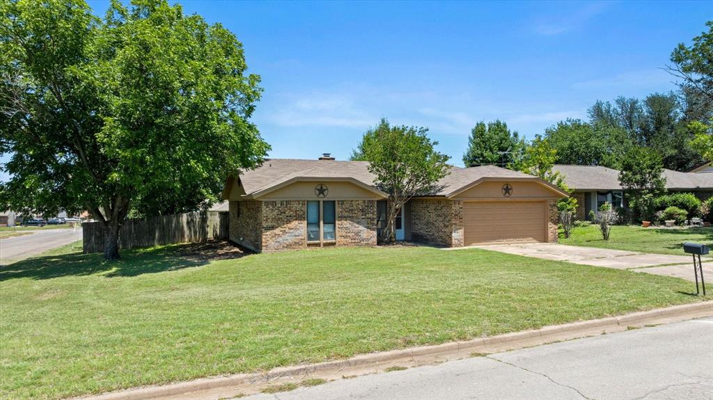 Brick home on a corner lot on the north side of Stephenville. Three bedrooms, two baths, split floor plan. Living room has wood beam ceilings, wood-burning fireplace, and opens into the dining area. Galley kitchen with oak cabinets and plenty of storage. Primary suite has two closets and a large double-sink vanity. Wood-look flooring throughout the main areas. Attached 2-car garage, open patio, and a good-sized yard with mature trees. City water, city sewer, Stephenville ISD. This home has great bones and tons of potential — priced to sell! Schedule your showing today!