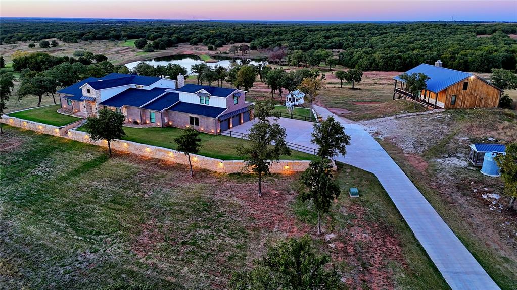 TURN-KEY LUXURY IN THE NORTH TEXAS HILL COUNTRY! Move-In ready 188 +- ac ranch retreat in Northern Montague County, located less than 1.5hours from DFW and strategically situated between the historic town of Nocona and the charming square of Saint Jo.  This property offers a 5008sf modern farmhouse main residence, a 1752sf guest cabin, a 102x60 workshop, livestock barn with working pens, rolling terrain, a gorgeous private lake with an additional two ponds, and a beautiful, gated entrance.  An upscale combination ranch of productivity and recreation has been captured, fused with the ideas of entertainment and full-time functionality in mind. The main home boasts 5 bedrooms, 5 full baths, two half baths, and a massive, “great room” with 24ft ceilings that is sure to impress.   High-end leathered granite, a full service beverage bar with wine fridge, ice maker, and walk-in fridge, commercial grade appliances, and dramatic lighting selections are just a few amenities you will notice.  Other perks include a home office with attached storm room, a wet-room, steam spa in the primary bath, a huge, custom walk-in closet, and an impressive outdoor patio experience complete with outdoor kitchen.  An idyllic, rustic themed guest cabin sits atop a hill overlooking the private lake below and is outfitted with an indoor-outdoor floor to ceiling rock fireplace, a 1000sf covered deck with wraparound porch, a saloon style bar, and two additional bed and baths for entertaining.  This is the ultimate guest experience and it is chalk full of details that won't go unnoticed along with the panoramic views.  The private lake features a fishing pier or dock if preferred and offers year-round recreational fun in the form of fishing, duck hunting, swimming, and more.  Deer feeder and stand will stay behind to encourage your own memories. An insulated shop with shed row, bunk house, bath, walk-in cooler, and hoist can be found just up the drive from the livestock barn and working pens.