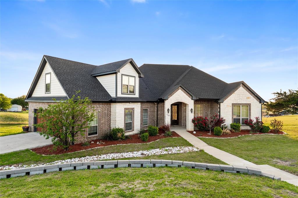 Set on a beautifully elevated homesite with sweeping views of open pasture and a peaceful pond, this thoughtfully designed home blends timeless finishes with a layout that truly lives well. Inside, rich hardwood flooring runs throughout the main living spaces, complemented by detailed crown molding, abundant natural light, and a stunning stone fireplace flanked by custom built-ins. The open-concept design connects seamlessly to the kitchen, where a large island with contrasting cabinetry, granite countertops, farmhouse sink, stainless appliances, and extensive storage make it both functional and visually striking—perfect for everyday living or hosting.

The primary suite offers a true retreat, featuring a spa-inspired bathroom with a freestanding soaking tub, oversized walk-in shower, dual vanities, and TWO spacious walk-in closets with built-ins. Closet not pictured doubles as a full storm shelter. Secondary bedrooms are generously sized with continued hardwood flooring and great natural light, while the oversized utility room is both practical and polished with ample cabinetry, folding space, and room to stay organized. Upstairs, a large bonus room provides flexible space for a media room, game room, or additional living area.

Outdoors, the covered back patio is a standout feature, finished with a warm wood ceiling, recessed lighting, and plenty of room to relax while taking in the expansive Texas views. The setting offers a rare combination of privacy and scenery, backing to wide-open land rather than neighboring homes. Additional highlights include propane gas servicing the fireplace, cooktop, and water heater, enhancing both efficiency and performance. This is a home that delivers space, comfort, and a setting that’s hard to find.