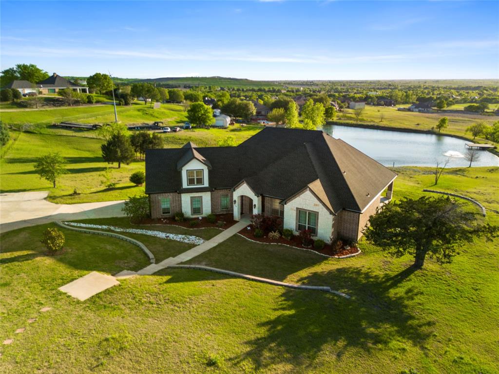 Set on a beautifully elevated homesite with sweeping views of open pasture and a peaceful pond, this thoughtfully designed home blends timeless finishes with a layout that truly lives well. Inside, rich hardwood flooring runs throughout the main living spaces, complemented by detailed crown molding, abundant natural light, and a stunning stone fireplace flanked by custom built-ins. The open-concept design connects seamlessly to the kitchen, where a large island with contrasting cabinetry, granite countertops, farmhouse sink, stainless appliances, and extensive storage make it both functional and visually striking—perfect for everyday living or hosting.

The primary suite offers a true retreat, featuring a spa-inspired bathroom with a freestanding soaking tub, oversized walk-in shower, dual vanities, and TWO spacious walk-in closets with built-ins. Closet not pictured doubles as a full storm shelter. Secondary bedrooms are generously sized with continued hardwood flooring and great natural light, while the oversized utility room is both practical and polished with ample cabinetry, folding space, and room to stay organized. Upstairs, a large bonus room provides flexible space for a media room, game room, or additional living area.

Outdoors, the covered back patio is a standout feature, finished with a warm wood ceiling, recessed lighting, and plenty of room to relax while taking in the expansive Texas views. The setting offers a rare combination of privacy and scenery, backing to wide-open land rather than neighboring homes. Additional highlights include propane gas servicing the fireplace, cooktop, and water heater, enhancing both efficiency and performance. This is a home that delivers space, comfort, and a setting that’s hard to find.