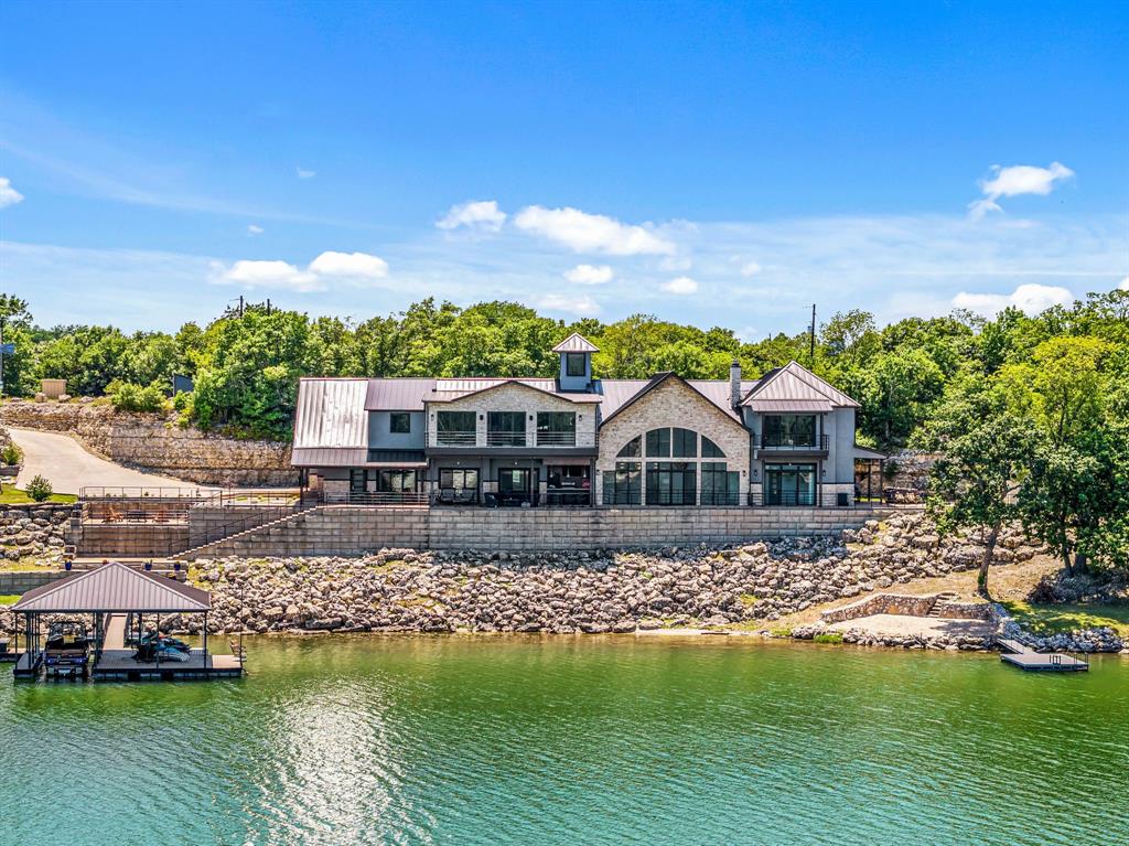 PRICE IMPROVEMENT!!! This Seller is ready to SELL!!! Truly unparalleled, private state-of-the-art lakefront estate situated on 1 acre with nearly 400 feet of pristine waterfront on beautiful Moss Lake. Designed for exceptional indoor and outdoor living, the home captures panoramic lake views from nearly every space and feature and expansive open-concept design with soaring ceilings and walls of glass! The gourmet kitchen is a true showpiece with top-of-the-line appliances, heated floors, a stunning all glass wine room and a hidden oversized pantry that also serves as a secure safe room. The primary suite is privately located on the main level with direct access to an outdoor patio complete with a fireplace and easy access to the beach area. The spa like primary bath features heated floors, a steam shower, coffee bar and custom cabinetry. A private staircase from the primary bedroom leads to a bonus living area with balcony overlooking the lake and a dedicated exercise room. Three spacious guest suites on the lower level each include private terrace access through sliding glass doors, their own bathroom and individual thermostats for ultimate comfort. Upstairs offers incredible entertaining space with a lakefront game room and private balcony, a fully equipped theatre room, and an impressive bunk room with eight queen beds and a loft, perfect for hosting large gatherings. The oversized heated floor garage provides ample room for multiple vehicles, boats and recreational toys. Outdoors, enjoy direct lake access with a Wahoo boat dock, expansive terraces and breathtaking waterfront scenery. Meticulously built by the seller himself with no expense spared, this extraordinary property offers craftmanship, luxury and amenities rarely found in one home. Truly a one-of-a-kind exquisite North Texas retreat with far too many features to list!