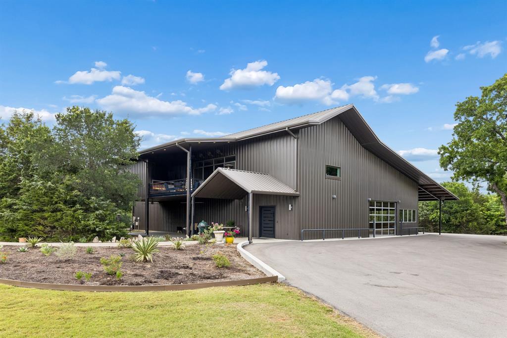 Set on 12.3 private acres, this meticulously designed estate offers a rare combination of luxury, functionality, and privacy. Behind custom gates, a curbed asphalt driveway winds past a picturesque pond before arriving at the property’s striking 7,102 square foot barndominium, completed in 2018 with exceptional attention to detail throughout. The main level features an expansive open living area with custom cabinetry, built-in double refrigerators, a pool table space, and a large full bath with separate his and hers restrooms. A custom iron staircase anchors the space, while an adjoining seating area creates a comfortable gathering point. Just beyond is the multi-purpose barn area with enclosed storage, secure workshop, and hidden office entry. The second level showcases soaring 20-foot vaulted ceilings and an open-concept layout centered around the living room and designer kitchen. Sliding doors open to a covered patio with a custom 10-foot gas fireplace overlooking the surrounding landscape. The kitchen is finished with exposed brick detailing, custom cabinetry, double refrigerators, dual walk-in pantries, oversized island, and farmhouse sink beneath a picture window with panoramic property views. The primary suite includes custom built-ins, exposed brick accents, spacious walk-in closet with integrated washer and dryer, and a luxurious bath featuring dual vanities, towel warmer, custom walk-in shower, soaking tub, and designer lighting. A secondary bedroom with full bath access completes the second floor, while a third-level flex space offers additional versatility. A short walk from the main residence, the 968 square foot cottage, completed in 2009, provides ideal guest accommodations with a covered porch, outdoor fireplace, 152 square foot casita, full kitchen, living area, and upstairs bedroom with full bath. Enhanced with solar panels and surrounded by lush wooded grounds, this one-of-a-kind property offers privacy, recreation, and refined country living.