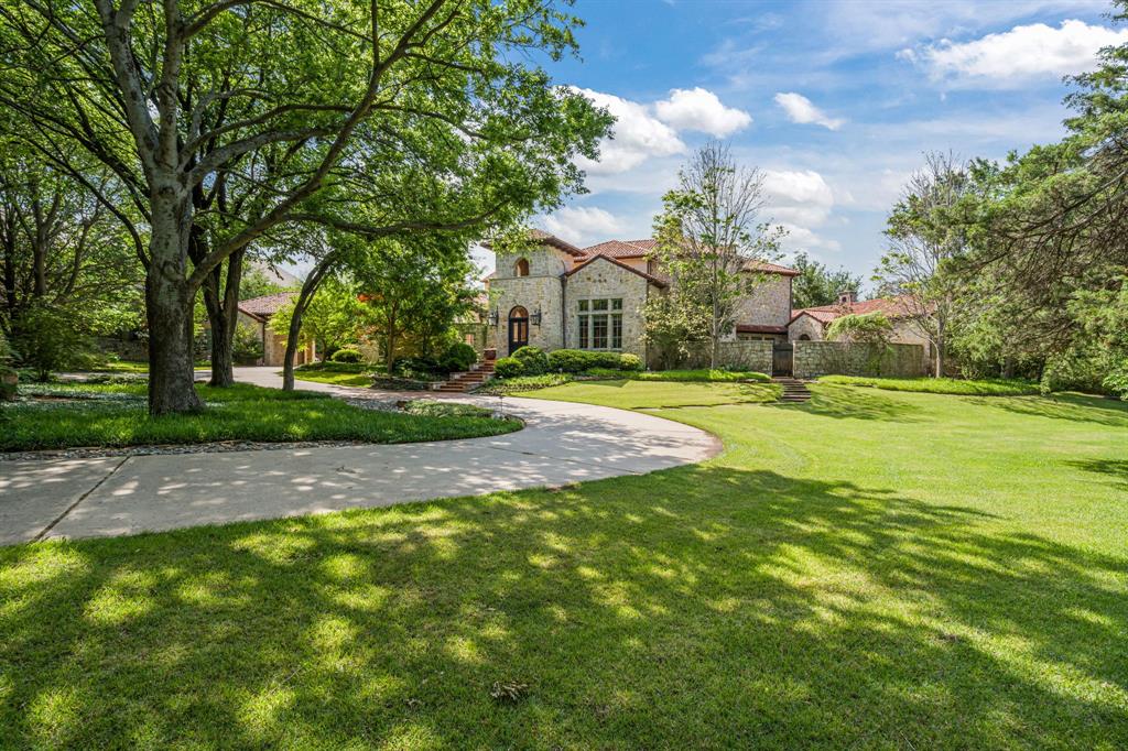 As you pass through the gates, ducks and turtles drift along the tranquil pond, offering an inviting glimpse of one of Southlake’s most exceptional properties. The drive winds beneath a canopy of mature trees, past broad lawns, before the home comes into view, nestled among seasonal foliage. Custom built by Cary Hy, this Spanish Colonial estate reflects timeless architecture with custom touches and designer-selected finishes including hardwood floors, French tile, marble counters, solid wood ceiling beams, and elegant lighting and hardware.
A private courtyard with a fireplace welcomes guests and establishes the calm, gracious tone carried throughout the home. Inside, views of the grounds unfold beyond the arched doors of the family room leading to the Claffey spa and infinity-edge pool. Thoughtfully designed for everyday ease, the first floor includes formal and casual dining areas, as well as a family room, music room, and media room, creating comfortable spaces for gathering and unwinding. Through antique pocket doors, the formal office overlooks both courtyards and includes a gas fireplace, and a second office is tucked away just beyond the kitchen.
The primary wing offers a private retreat with its own courtyard, exercise room overlooking the pool, and a spa-inspired bedroom with fireplace and en-suite bath. The kitchen is well appointed with a marble-topped island, Wolf, Sub-Zero, and Miele appliances, and is supported by a walk-in pantry, butler’s pantry, bar, wine room, oversized laundry, and pet room. A generous guest suite with direct access to the front courtyard completes the main level.
Upstairs, three private ensuite bedrooms are joined by an additional family room with bar and powder bath, along with a media room that can be converted to a sixth ensuite bedroom. Outdoors, a covered living center with gas fireplace, grilling station, and kitchen island extends the living space, complemented by a pool, spa, firepit, sports court, and expansive lawn.