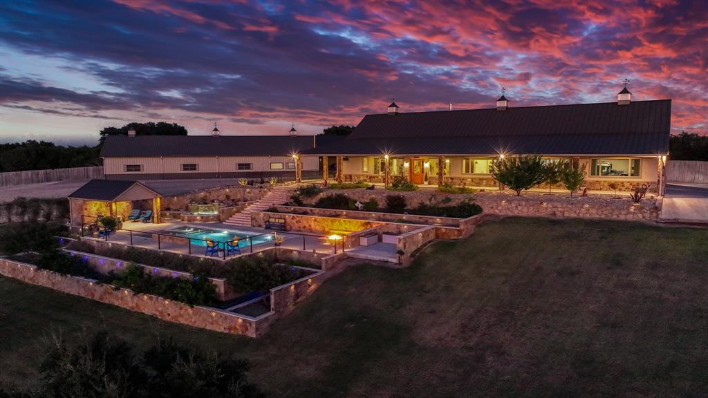 **CONTINUE TO SHOW**  Enjoy breathtaking sunsets and million dollar views from this stunning 110(+-) acre ranch with a 2021 Will Steed custom home perched high on a hill. The 4 BR, 2.5BA residence offers so many extra amenities including expansive windows that frame sweeping views of the rolling landscape, a metal roof and foam insulation for excellent energy efficiency. The oversized climate controlled garage features a tornado shelter bolted to the foundation plus a secure hidden gun room. Outdoor living is unmatched with a covered porch, side outdoor kitchen, sitting area with a fireplace, and a custom resort style pool with a motorized cover, cabana, (custom drain system flows downhill to pond), large gas fire pit, built in hot tub and a peaceful water feature perfect for relaxing or entertaining while watching the sun set over your land. LED custom lighting on all tiers of remarkable front landscaping design. Property includes a very nice 10' x 10' greenhouse, and a 13.7' x 30' workshop. The spacious Barndominium includes a fully insulated 58 x 36 large shop area with a large overhead door, stairway to a loft storage including a hoist and plenty of room for storage or equipment. The Barndominium also has an attached, enclosed 14' x 100' side barn, a 30' x 36' carport and a very nicely finished 1,500 sq.ft. living area with two bedrooms, living room, a craft or office space, a full kitchen with a nice breakfast bar. The property has excellent perimeter fencing, also cross fenced for horses, cattle, sheep or goats, with 4 automatic fill water troughs, multiple barns, three stock ponds plus a seasonal creek and a retaining pond. Majestic oaks dot the landscape, providing shade and beauty throughout. The private road from the highway is well maintained and leads to this amazing home and property that have been meticulously cared for. This exceptional ranch is a rare opportunity to own a property that blends luxury, functionality, and the authentic Texas lifestyle.