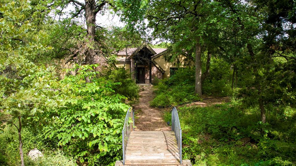 You'll love this spacious home in Oak Point, TX. Nestled on 1.65 heavily wooded acres in the prestigious Emerald Sound community, this custom 4-bedroom, 3-bath estate offers over 4,100 sq. ft. of living space with unlimited potential. Privately situated with a grand bridge walkway entry, the home is surrounded by a state-recognized wildflower landscape & meandering garden paths, creating a serene retreat reminiscent of old-world European charm.
Inside, cathedral ceilings, Tiffany-style lighting, & rich wood flooring set an elegant tone, while natural light pours through expansive windows. The chef's kitchen is appointed with Corian countertops, a large island, & an abundance of built-in cabinetry. The primary suite features a private en-suite with a jetted tub, dual vanities, & custom closet system. Entertain effortlessly with a spacious living and dining area, a screened sunroom, built-in's throughout, & multiple balconies offering peaceful treetop views. The basement includes a bonus room, mudroom, & two additional bedrooms, perfect for guests or multigenerational living.
Additional highlights include a 3-car oversized garage (24x41), central vacuum, propane fireplace, smart layout with dedicated office, and premium features throughout. Enjoy the peace of country living with the convenience of being near Lake Lewisville and top-rated Denton ISD schools. This unique home is ready for you to make it your own.
