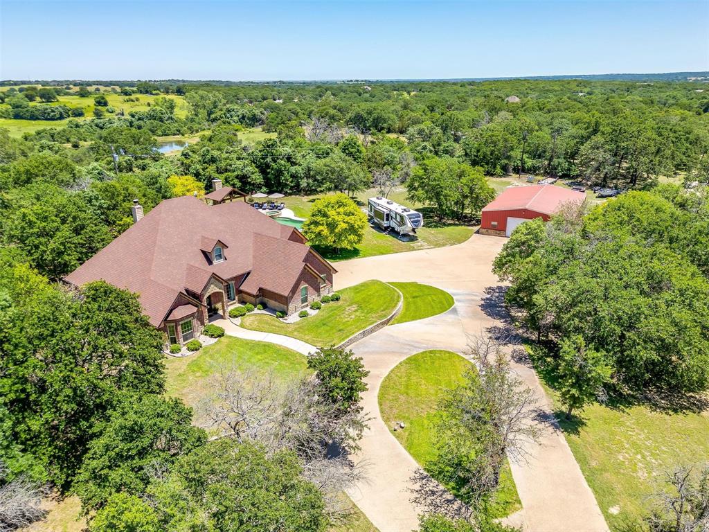 PRICE IMPROVEMENT + 1% LENDER CREDIT TOWARD RATE BUYDOWN WITH PREFERRED LENDER ~ If you’ve been waiting for land, luxury, privacy, and versatility in one property—this is it. Nestled on 4+ private, tree-covered acres behind the gates of an exclusive community, this custom-built and extensively remodeled Texas ranch estate offers a rare combination of wide-open space, resort-style outdoor living, equestrian flexibility, and high-end finishes. Inside, soaring ceilings, rich hardwood floors, custom millwork, and expansive windows create a light-filled open-concept layout with peaceful acreage views from nearly every room. The home is designed for both everyday comfort and effortless entertaining. The chef’s kitchen features imported Taj Mahal quartzite countertops from Brazil, gas cooktop, double ovens, built-in refrigerator, brick architectural accents, custom cabinetry, and generous prep space designed for hosting with ease. The primary suite is a relaxing retreat with spa-inspired bath, separate shower, and walk-in closet. Three additional bedrooms, 2.5 baths, and an upstairs game room offer flexible use for guests, media, fitness, office, or play. A dedicated Doggy Suite adds thoughtful functionality for pet lovers. Step outside to a true resort-style backyard: covered living area with wood-burning fireplace, beach-entry pool, spa, and expansive patios perfect for entertaining or unwinding. The acreage beyond delivers true Texas living—seasonal private pond, horseback riding, gardening, wildlife watching, and stunning sunset views. Equestrian-friendly land offers room to roam, ride, and expand. The 40x60 shop is plumbed for a bathroom and includes its own aerobic septic system—ideal for a home business, gym, workshop, or future conversion - and adds storage, livestock capability, equipment space, or potential guest quarters. Gated entry, mature trees, expansive driveway, and peaceful country setting with convenient access to town. Luxury like this is hard to find!