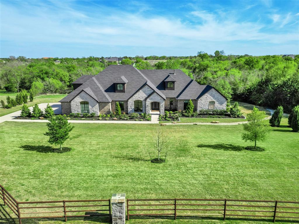 In The Prestigious Hills of Lone Star – where country is the theme for easy living. Set against a beautiful tree-lined backdrop, this property offers privacy and generous elbow room. Thoughtfully designed with over 7,300 sq. ft., including more than 5,000 sq. ft. on the first level, this home was made for entertaining. The expansive kitchen is the heart of the home and is complete with every convenience for the cook, including a large entertaining island, gas cooktop, private dining area, scullery kitchen, and generous walk-in pantry. Open to the great room is a beautifully appointed wet bar room, creating a natural gathering space with lovely backyard views—perfect for making memories with friends and family. The private owner’s suite features a separate sitting area, peaceful views, a Texas-sized bath, and separate closets. Three additional guest suites with private baths are located on the main level, including a mother-in-law suite with its own sitting room. Greet the morning with coffee or spend a quiet afternoon in the nature-filled sunroom located off the secondary living-flex space with fireplace. Completing the first level are a private study and a spacious utility room with space for multiple washer and dryer sets. Step outside under the Texas sky and enjoy year-round living with a covered patio, built-in outdoor kitchen with smoker, and an enormous pool-ready backyard. The second level becomes a destination for relaxation and fun, featuring a spacious game and living area, flex room, oversized wet bar for entertaining, and a large balcony perfect for watching both sunrise and sunset. A second flex area is ready for a private gym, additional storage, or play space. This is a smart home that also includes a four-car garage and abundant storage throughout. When you are ready for a night out, take a short country drive to Celina or downtown McKinney, where the food is fabulous, and the shopping is fun.