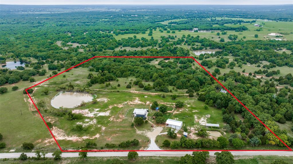 Escape the city for this stunning 25 acre retreat featuring rolling hills, a scenic pond, & total privacy. This 2019 custom built home combines modern efficiency with rustic charm, boasting spray foam insulation, a metal roof & private well. The foundation was poured with reinforced peers! Relax on the massive wrap around porch with swings overlooking the water or enjoy the outdoor kitchen. Inside, vaulted ceilings frame an open concept living area & a gourmet kitchen with a large island, gas cooktop, & farmhouse sink. The primary suite is a main floor with a deep garden tub, tiled shower, & a functional laundry room. Each spacious bedroom features its own private bathroom, ensuring comfort for guests. Hideout bunker or kids playroom is under the stairway. Enjoy a 30x40 powered shop with oversized doors as your garage. It complements the barn & Ag Wildlife-exempt land, perfect for horses or cattle. Located outside city limits, you have the freedom to enjoy fireworks and recreation on your own terms. This property offers the perfect blend of luxury, utility, and country freedom.
