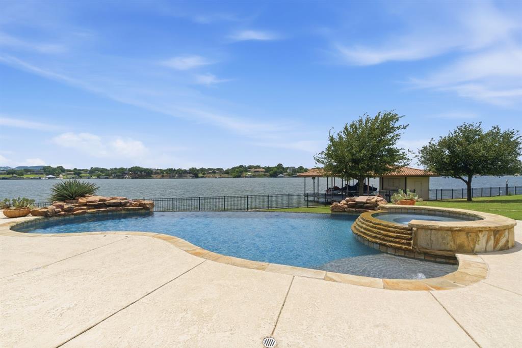 Wake up to shimmering water views, spend your afternoons poolside, & end each evening with unforgettable sunsets dancing across the lake. Set beside the sparkling waters of Lake Granbury, this extraordinary Mediterranean-inspired estate offers resort style living. Situated on a premier walk-out waterfront cul-de-sac lot within the gated Catalina Bay community, the home was designed to capture the beauty of its surroundings from nearly every room. Expansive walls of windows frame breathtaking lake views & fill the home with natural light, while rich wood floors, soaring cathedral beamed ceilings, curved hand-troweled walls, arched doorways, & extensive moldings create an atmosphere of timeless elegance. The gorgeous kitchen features a massive island, abundant workspace, & a dry bar overlooking the open dining area. The expansive living room is anchored by a stunning  floor-to-ceiling stone gas fireplace, creating a warm & inviting setting while showcasing spectacular lake views beyond with a full wall of budded glass windows. The massive primary suite offers a private sitting area, panoramic lake views, & a luxurious spa-like bath featuring an arched ceiling, columns, soaking tub, walk-in shower, & remarkable double walk-in closets. 2 generous & private split guest rooms. An exceptional study with custom built-ins is the perfect space for a personal library, office, or flexibility as a 4th bedroom. The heart of the outdoor living experience is an infinity-edge pool & spa that appear to spill seamlessly into the lake. Gather with friends around the outdoor kitchen & fireplace, enjoy dinner beneath the stars on the covered patio, or stroll across the lush lawn to your private dock for an evening cruise on the lake. With exceptional craftsmanship & one of the most captivating waterfront settings on Lake Granbury, this is more than a home, it is a destination for making memories, celebrating life's moments, & embracing the lakefront lifestyle you've always imagined.