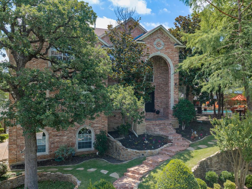 Positioned on a generous corner lot in Colleyville’s Saddlebrook neighborhood, 4105 Inwood Lane delivers approximately 4,863 square feet with five bedrooms, five full baths, one half bath, three levels of living space, and the uncommon advantage of a finished basement. A stately brick exterior, arched entrance, stone detailing, mature trees, and layered landscaping create striking curb appeal.

Inside, expansive windows, tall ceilings, and an open upper landing fill the home with natural light. The main floor offers formal living and dining areas, a spacious family room with a fireplace and built-in cabinetry, and a well-equipped kitchen featuring abundant white cabinetry, dark countertops, a center island, double ovens, and direct access to the patio deck. The private primary suite is also located on the first floor.

Four additional bedrooms are upstairs, including two with private en-suite baths, providing flexible accommodations for overnight guests, workspaces, or everyday living. The finished basement adds exceptional versatility with a large recreation area, wet bar, and room for games, fitness equipment, hobbies, or an office. A separate theater creates a dedicated space for movie nights and entertainment.

The backyard feels like a private resort beneath a canopy of mature trees. A sparkling pool and spa are complemented by a rock waterfall, natural stone decking, a gazebo, several seating areas, and plenty of room for outdoor dining and gatherings.

The property is served by Grapevine-Colleyville ISD and is located just steps from Sparger Park, an eight-acre green space with a covered pavilion, playground, picnic areas, open recreation space, restrooms, a half-mile multi-use trail, and POW Memorial. The Colleyville Nature Center offers additional trails, ponds, fishing, a playground, pavilion, pier, and amphitheater. Highway 121 and the shopping, restaurants, and entertainment at Glade Parks are less than ten minutes from the home.