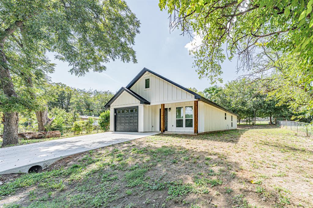 Welcome to your brand-new modern farmhouse retreat just blocks from Lake Granbury and minutes from the charm of Historic Downtown. Designed with today’s lifestyle in mind, this home blends clean architectural lines with thoughtful details throughout.

Inside, soaring vaulted ceilings and an open-concept layout fill the living spaces with natural light. The gourmet kitchen showcases high-quality wood cabinetry, tons of counter space, plenty of cabinets for storage, and a large island perfect for entertaining. A walk-in pantry provides even more space and organization. The kitchen comes complete with stainless steel appliances, including the refrigerator, making it both beautiful and functional. The living room impresses with its dramatic ceiling height, decorative lighting, and a sleek iron ladder that leads up to a bonus loft space enhanced by a live-edge wood bench that adds warmth, function, and a unique touch of character.

The primary suite is a true escape with its spa-inspired bath, featuring custom tilework, granite vanity, and abundant storage. The entire home is finished with arrow-design wood-look tile flooring, complemented by ceiling fans and decorative lighting throughout.

Outside, you’ll find a wide driveway, a covered front porch, and a rear patio that expands your outdoor living options. The generous backyard is ready for relaxation or play. Built with foam insulation for comfort and efficiency, along with a new septic system that irrigates the yard, this home offers peace of mind and long-term savings.

Whether you’re envisioning it as your first home, a lake getaway, or an investment property with Airbnb potential, this home’s location and design make it a standout choice just blocks from the water and minutes from downtown. Come experience for yourself all the extras that make this home stand out.