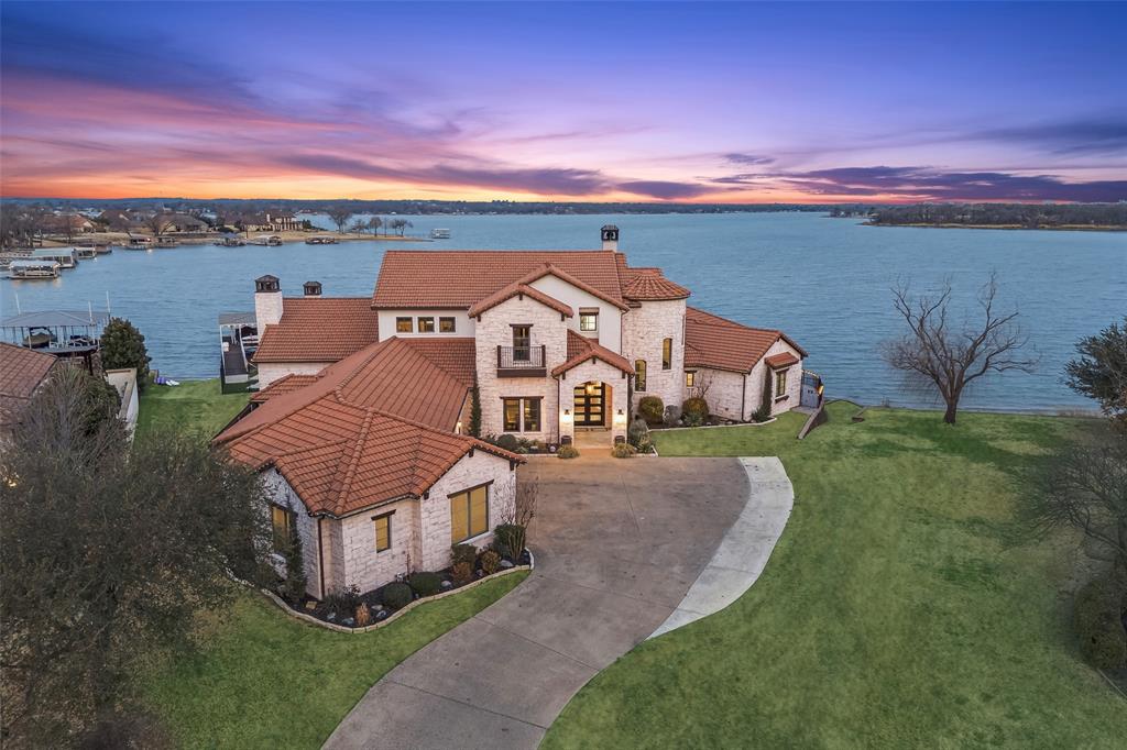 Poised on the open waters of Gated Resort on Eagle Mountain Lake, this extraordinary, one-of-a-kind custom estate defines lakefront luxury. Designed for those who expect the exceptional w-sweeping lake views through dramatic walls of glass, refined architectural details & seamless indoor-outdoor living that rivals the finest private resorts. Grand living is nothing short of spectacular. The open concept flows effortlessly into the dining area & expansive covered patio, creating a breathtaking backdrop for everyday living & unforgettable entertaining. Gourmet kitchen is a showpiece, outfitted w-Fisher & Paykel professional range, Monogram commercial-grade refrigeration, gas cooktop w-griddle, dual dishwashers + an oversized island. Primary suite is a private sanctuary, tucked away on the main level w-stunning lake views, a spacious sitting area, tiered ceilings w-wood beams + direct access to the patio. The spa-inspired ensuite bath is magazine-worthy! A secondary guest suite on the main level offers its own ensuite bath for elevated guest comfort. Exceptional main-level amenities include an executive study, a full pool bath w-direct outdoor access, a well-appointed laundry room w-electronic dog door & private dog run & a state-of-the-art golf simulator room. Upstairs, 3 generously sized bedrooms each feature private ensuite baths along w-a balcony capturing breathtaking lake views. The private theater room delivers a true cinematic experience w-luxury seating w-heating, cooling + motion features. The outdoor living experience is unparalleled. Two oversized patios w-electric drop-down screens, a wood-fired pizza oven, outdoor fireplace, covered pergola + a resort-style pool create the ultimate lakeside retreat. A private dock w-one boat & two jet ski lifts + a floating dock places open-water adventure just steps away. Nestled on a quiet cul-de-sac in a 24-hour gated community, Eagle Mountain Resort offers an 18-hole championship golf course & resort-style amenities.