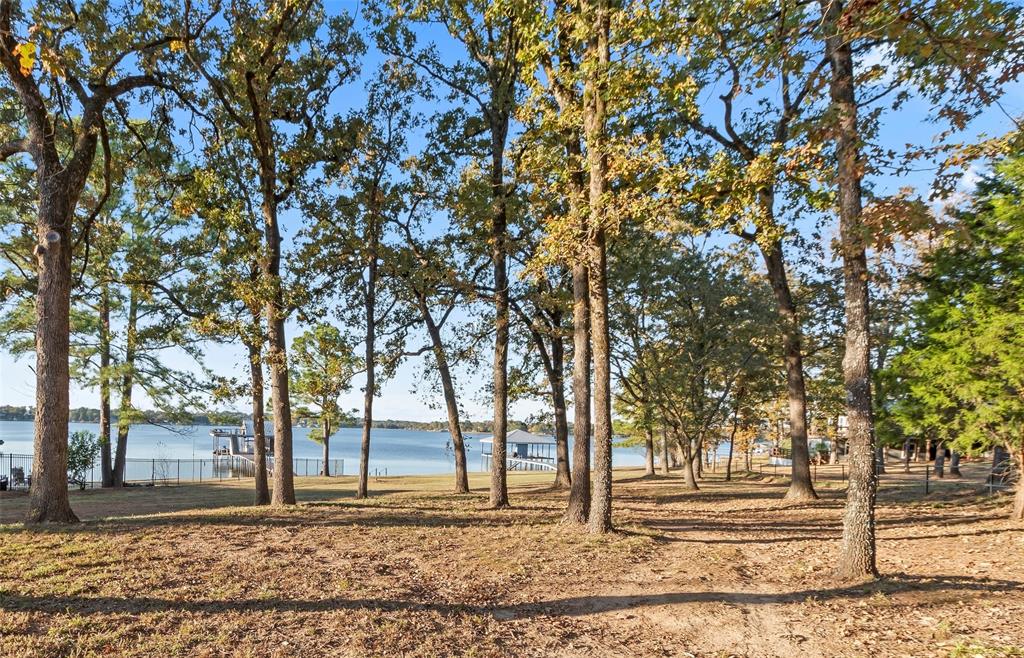 Cozy lake cottage on 3.4 acres with nearly 200 ft of waterfront, great water depth, and a brand-new top-of-the-line boathouse! Charming 1,104 sq. ft. home ideal as a weekend getaway or a place to stay while building your dream Lakehouse. The existing residence can easily become a future guest house for family and friends. Sellers have custom 5,531 sq. ft., 5 bed, 6.5 bath, 3-car garage house plans already drawn up for the property, and they’re included in the list price—making it even easier to bring your vision to life. The property is fully fenced with a gated entry and offers lots of buildable land surrounded by mature trees for privacy and space. No known restrictions—so there’s potential for multiple homes (with county permit for septic system(s), livestock, or even short-term rentals. Inside, the home has been freshly painted for a bright, light, and inviting feel. The living area features a wood-burning fireplace and large picture window overlooking the property and open water. The home’s elevated position provides beautiful lake views from both the living room and kitchen. The kitchen includes granite countertops, stainless appliances, newer-style cabinets, crown molding throughout, and tile floors (no carpet). A huge covered deck extends the living space outdoors—ideal for relaxing or entertaining. Outbuildings include a large RV-boat barn that can accommodate multiple vehicles, a two-bay metal barn with enclosed shed area, plus two tool sheds. Plenty of room to add a large metal building, livestock barn, or barndominium! Livestock allowed per acre within Henderson County restrictions. The new boathouse is a showstopper—built with all-aluminum decking that’s low-maintenance, cool to the touch on hot days, and never needs staining or painting. It includes a wide walkway, boat and jet ski lifts, and a massive covered seating area perfect for lakeside gatherings. A rare waterfront find offering acreage, great water depth, and upgraded boathouse.