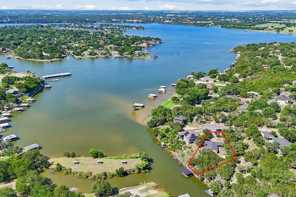 Perched above the tranquil waters of Lake Granbury, this inviting waterfront retreat offers breathtaking views, a private covered boat dock, and the peaceful charm of lakeside living. Tucked away on a quiet cul-de-sac within the gated community of Indian Harbor, this property is the perfect place to slow down, unwind, and enjoy life on the water. Inside, soaring vaulted ceilings and a dramatic floor-to-ceiling stone fireplace create a warm and welcoming gathering space. Expansive windows frame stunning lake views and fill the home with natural light, while the open-concept layout makes entertaining effortless. The kitchen features abundant cabinetry, generous workspace, and a breakfast bar overlooking the living and dining areas.
The primary suite captures peaceful water views and provides a relaxing escape at the end of the day. Additional bedrooms offer flexibility for guests, family, or a home office. Throughout the home, comfort and functionality blend seamlessly with the incredible natural beauty just beyond the windows.
Step outside and discover what truly makes this property special. Multiple decks and covered outdoor living spaces provide front-row seats to sparkling water views, colorful sunsets, and gentle lake breezes. A stairway leads to the private covered boat dock, offering easy access to boating, fishing, kayaking, and endless days on Lake Granbury. Mature trees, natural landscaping, and a rock seawall enhance the property's privacy and timeless lake-house appeal. Whether you're searching for a full-time residence, weekend getaway, or investment opportunity, this waterfront property offers a rare chance to enjoy the relaxed lifestyle and unforgettable views that make Lake Granbury such a treasured destination. Conveniently located just minutes from Granbury's historic square, dining, shopping, and entertainment, this lakeside retreat is ready to be enjoyed.