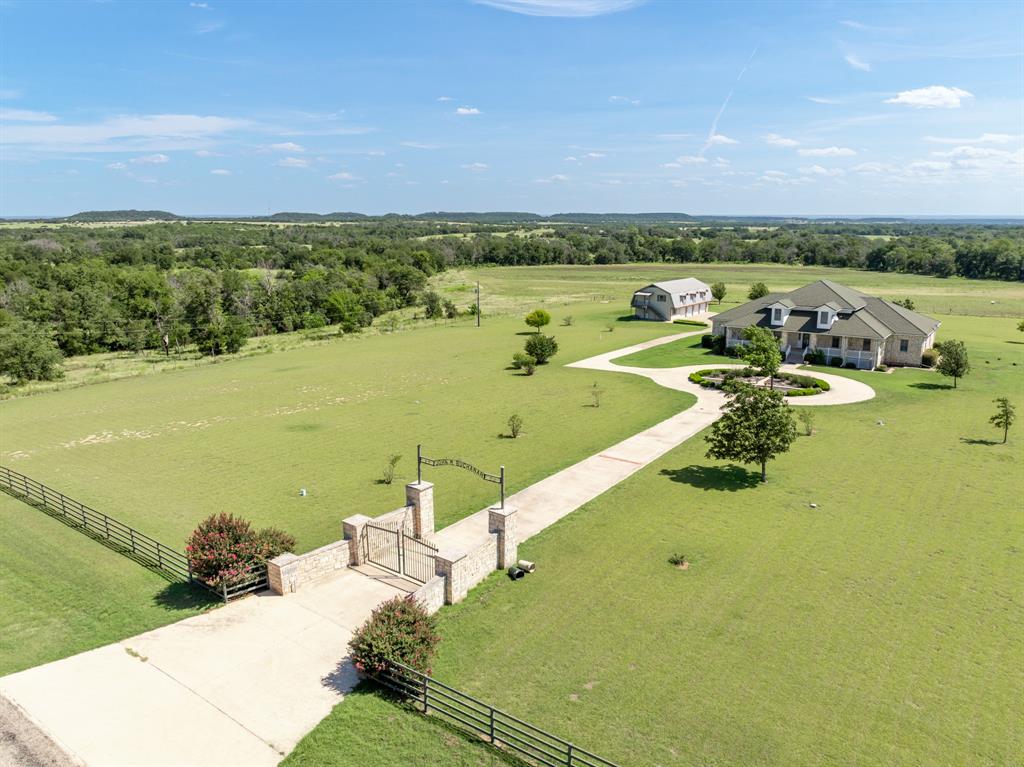 Located just west of Clifton on paved FM 182, this 7 acre estate offers privacy in Bosque County. Only 8 miles from Clifton, with a hospital, shopping, dining, and schools, the property is conveniently located, offering 45 minutes to Waco and 2 hours to Dallas–Fort Worth.

The custom Colonial-style home, built in 2000, features a roundabout drive and grand two-story design with approx. 3,620 sq. ft. on the main level and 1,715 sq. ft. upstairs. The first floor features a formal living and dining area, a spacious kitchen equipped with double ovens, an electric range, and a commercial-size refrigerator & freezer, as well as a large family room. Also on this level are two bedrooms, one of which is used as an office, an oversized laundry room, and the primary suite with two full bathrooms, one featuring a clawfoot tub and the other a walk-in shower.

Upstairs, the property offers five bedrooms and two bathrooms. Covered front and back porches capture sweeping views of the hillside.
Additional improvements include a four-car garage with a 1,800 sq. ft. apartment with 2BR & 2BA and a 3,200 sq. ft. metal shop with a holding tank. Two water wells and a septic system service both the home and apartment.

Surrounded by large ranches, this property offers a blend of privacy, space, and accessibility, an ideal retreat for those seeking a serene country lifestyle within easy reach of Clifton and the greater Bosque County area.