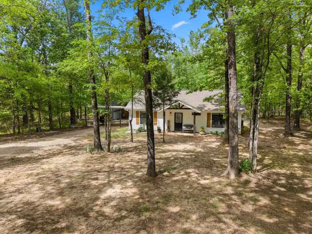Affordable Lake Fork home…move-in ready! This well-built well-maintained 2-bedroom, 1-bath home is nestled among towering trees and surrounded by abundant wildlife, including deer, foxes, and a variety of birds. The charming layout features an open-concept living, dining, and kitchen area, with a wall of windows along the back that fills the home with natural light and offers a peaceful view of the woods. Step outside to the covered back porch and enjoy the privacy and serenity this property provides. The bright, inviting kitchen boasts painted custom cabinetry, beautiful granite countertops, and stainless-steel appliances. Luxury vinyl flooring runs throughout the main living areas, while both bedrooms feature stained concrete. A convenient stackable washer and dryer are tucked into a closet just off the spacious foyer. The bathroom also showcases granite countertops and a custom tile tub and shower. This property is considered waterfront to Lake Fork and includes SRA leaseback. While the waterfront is very marginal, a pier could be built to enjoy fishing access. Additional improvements include a recently added metal I-beam constructed 3-sided outbuilding with a concrete floor—ideal for storage, workspace, or easily finishing out the front side to create an enclosed garage. Located in a quiet community with a private boat ramp for homeowners, this is a rare opportunity to own a well-maintained home on Lake Fork at an affordable price. Schedule your showing today!