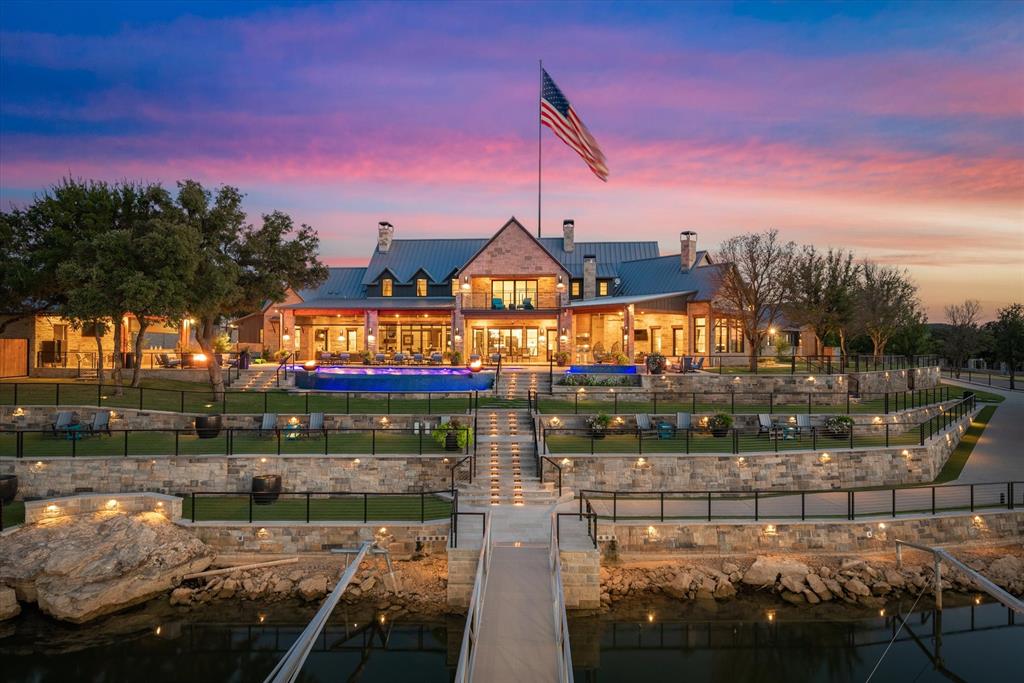 Indulge in the epitome of luxury within this exceptional lakefront residence. Step inside and discover a breathtaking array of premium features with the soaring vaulted ceilings, immersive Dolby Surround Sound, and abundant natural light pouring in through the large windows. The chef's dream kitchen boasts a 6-burner range, three ovens, two significantly large islands with 2 sinks, and a Miele coffee station. The primary suite, with its cozy fireplace, serves as a serene sanctuary, complete with a separate living area, standalone tub, and a soothing waterfall shower. Four other dedicated guest suites offer an array of amenities at the touch of a remote control. The media room impresses with its remarkable sound system, while the bunkroom provides a premier view, ideal for accommodating guests. Step into outdoor bliss with expansive living space that features a stunning infinity edge pool and spa, a commercial pizza oven, automated shades, and a fully equipped dock for water activities.