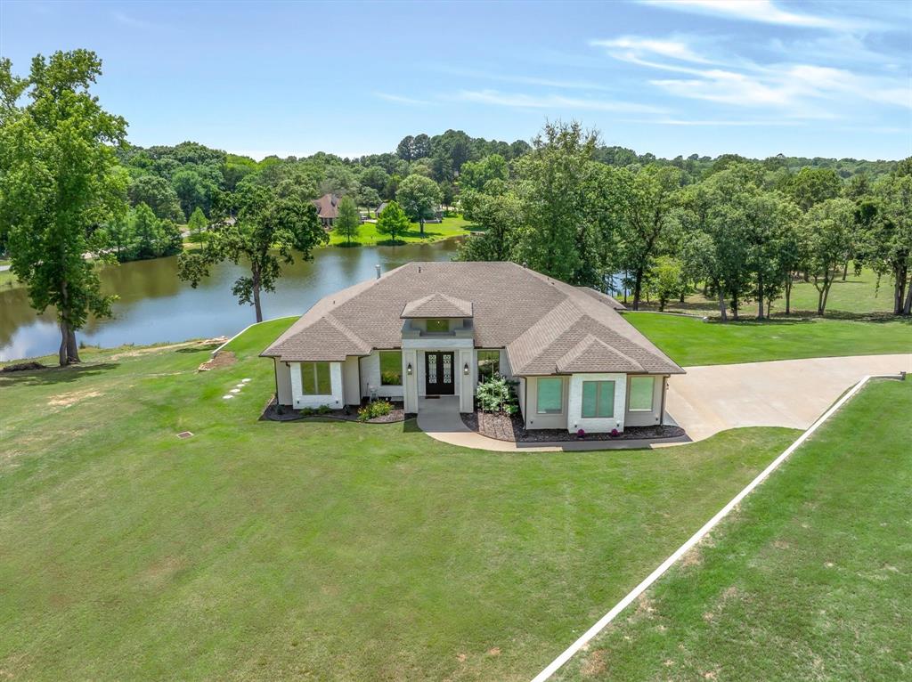 A serene lakefront retreat in private Tuscany Lake Estates, this 2,258 SF 2019-built home sits on 1.22 acres overlooking a private, spring-fed lake that maintains beautiful water levels year-round. Nestled on a gentle hill in a peaceful community of quality homes, it offers big-water views, gorgeous sunsets, & everyday moments surrounded by nature. Inside, an open-concept living & kitchen area frames the lake like artwork, with an electric fireplace & walls of windows drawing your eye straight to the water. The kitchen features a large quartz island with breakfast bar, beautiful countertops, glass-front cabinetry, & a cozy café-style breakfast nook with a built-in window seat where you can watch wildlife on the lake with your morning coffee.  The private primary suite is a true retreat with lake views, direct access to the covered patio, & a spa-like ensuite bath—featuring a large walk-in shower with seat and dual shower heads, a soaker jet tub, dual vanities, a walk-in closet that includes a framed, lighted shadow box perfect for a wedding dress or special display piece. Three separate bedrooms on the opposite side of the home, 2 additional full baths, & a dedicated office with custom glass French doors provide plenty of space & flexibility for family, guests, or working from home. Thoughtful extras are everywhere: glam decorative lighting, electric window coverings, a formal dining room, 3-car garage, sprinkler system, and a long driveway with ample guest parking. Outside, the beautifully landscaped yard flows down to the water’s edge, where you’ll find a fire pit area, pier, creating a wonderful setting for fishing the stocked lake, evenings by the fire, or simply unwinding on the large, covered patio with your grill.  Located just outside the city limits yet only mins from all the charm & amenities of nostalgic Mineola—with its boutiques, dining, and historic downtown—this lakefront home blends quiet country feel with convenient access to town.