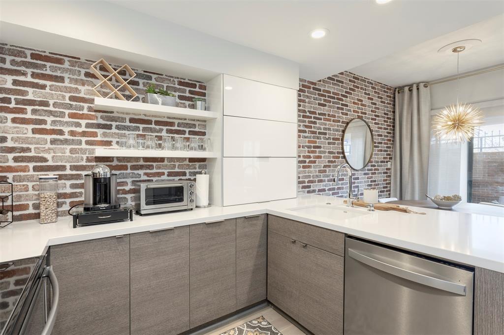 Experience refined living in this exquisite 1-bedroom, 1.5-bath residence thoughtfully renovated and located in the coveted Boardwalk on the Parkway community. Positioned on the first floor, this sophisticated condominium offers 985 square feet of curated interiors where timeless comfort meets modern design. The chef-inspired kitchen is a true showpiece, featuring custom cabinetry including horizontal bifold cabinets, dramatic waterfall-edge countertops at the peninsula, and a striking brick-style backsplash that seamlessly extends into the dining space—creating a cohesive, high-end aesthetic. Thoughtful details continue with modern barn-style doors concealing the pantry and stackable washer and dryer, blending function with architectural interest. The living area exudes warmth and elegance, anchored by a wood-burning fireplace and enhanced by built-in shelving, a wet bar, dual pane low-e windows and abundant storage—ideal for both intimate evenings and elevated entertaining. Step outside to your private, fenced patio, a serene retreat perfect for morning espresso or evening wine. Residents enjoy access to a sparkling community pool, manicured grounds, and the convenience of an enclosed carport with additional storage. Ideally situated in North Dallas near premier shopping, dining, and major highways, this home delivers a lock-and-leave lifestyle without sacrificing sophistication, comfort, or location.