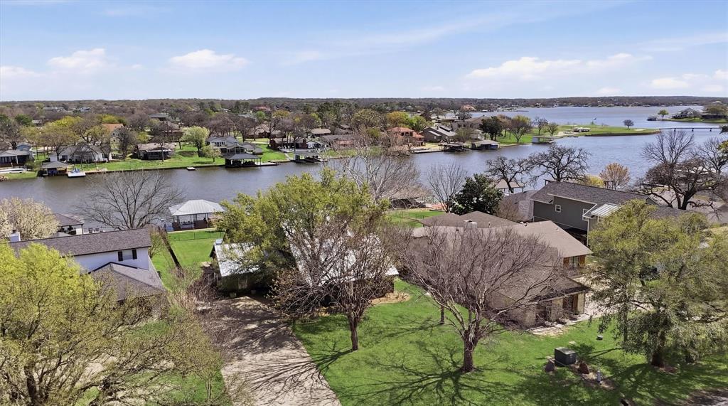 Discover this beautifully updated lakefront home on the desirable west side, offering stunning water views, a screened-in porch, and exceptional outdoor living spaces—including a fire pit and private boat dock. Tastefully updated inside, the home features a stylish kitchen with custom cabinetry, granite countertops, and a spacious island. All bathrooms have been tastefully modernized, and the home is finished with wood-look tile flooring throughout, plantation shutters, and updated lighting. The main living area boasts cathedral ceilings and a striking rock wood-burning fireplace. It opens seamlessly into a bright sunroom with floor-to-ceiling windows that frame gorgeous lake views and fill the space with natural light. The home offers 3 bedrooms and 3 full bathrooms, including a convenient downstairs bedroom and bath. The upstairs primary suite includes an ensuite bath with a large stand-alone shower. The third bedroom currently features four built-in bunks but easily accommodates a king bed or two full beds if preferred. Step outside to the expansive screened-in porch that leads to the backyard and private dock. The dock includes a boat lift and plenty of room for relaxing by the water. A lakeside deck with a fire pit creates the perfect setting for evening gatherings under the stars. With the backyard facing east, you’ll enjoy relief from the hot Texas sun in the afternoons and evenings. The front yard is dotted with mature trees, and the long driveway provides ample parking. The garage also includes an air-conditioned workshop space. Whether you're enjoying summer lake activities, relaxing on the porch, or watching the 4th of July fireworks over the dam, this home is designed for year-round enjoyment. Ideal as a full-time residence or vacation retreat, lakefront homes of this quality and price are rare—especially with the added amenities Lake Kiowa offers. Your opportunity to enjoy lake living is here. Come take a look!