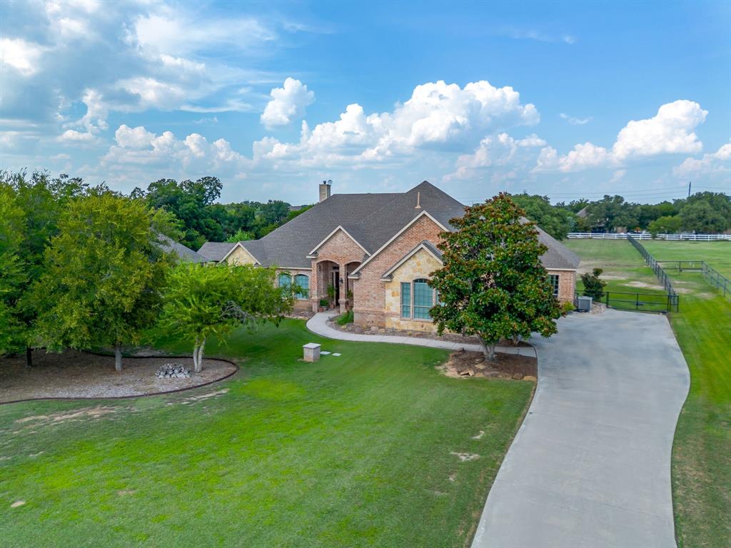 Escape to this stunning custom home on a sprawling one-acre lot, where luxury and country living blend seamlessly. This beautiful one-story brick home, with its elegant stone accents and majestic mature trees, boasts stunning curb appeal. Step inside and be greeted by the warm glow of rich, hand-scraped hardwood floors that flow into the formal dining room and cozy living area featuring a striking fireplace. The heart of the home is a chef’s kitchen designed for both culinary artistry and daily life, featuring a stainless steel double oven, gas cooktop with pot filler, ample cabinets, tumbled stone backsplash, and granite countertops anchored by a large central island.  A spacious built-in bench seat in the breakfast nook is the perfect spot for casual meals, while floor-to-ceiling windows flood the space with natural light and offer serene views of the backyard. This home is perfect for both entertaining and comfortable daily living, with vaulted ceilings, elegant crown molding, built-in cabinetry, and graceful arches. An ideally located mud room area provides access to the backyard patio, a full bath and guest room, an oversized garage, and a utility with sink & extra storage. The Perfect private space for in-laws, guests, older children, or a separate telecommuting office. Outside, the large covered patio is an ideal spot to relax and take in the natural beauty this neighborhood offers. The expansive yard offers endless possibilities, with ample room for a pool, playsets, and gardens. A three-car side-entry garage and generous parking provide space for all your vehicles, with room to add a Shop with RV, boat, and ATV parking.  Located approximately 35 minutes from Downtown Fort Worth, 25 minutes from Lockheed Martin and the Naval Air Station Joint Reserve Base, and just 10 minutes from Eagle Mountain Lake Twin Points and Fort Worth Nature Center, this home offers a quiet escape with convenient access to city amenities and outdoor recreation.