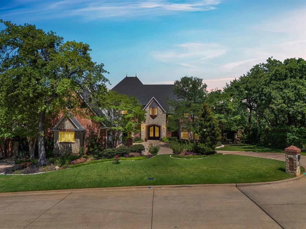Tucked within the private enclave of Vanguard Estates, this stunning 6,502 SF Colleyville home delivers unmatched craftsmanship and effortless luxury at every turn. Soaring ceilings, hand-scraped hardwood floors, and custom millwork set the tone from the moment you step through the ornate iron-and-glass double doors. The grand foyer opens to an elegant formal dining room with plaster medallion ceiling and designer chandelier, and a wood-paneled formal living room with coffered ceiling, carved marble fireplace, and French doors to the exterior. At the heart of the home, the chef's kitchen is a masterpiece — Fulgor Milano 6-burner range, double ovens, SubZero refrigerator, Miele dishwasher, pot filler, and quartzite islands — flowing seamlessly into the cathedral great room where soaring timber trusses frame a floor-to-ceiling stone fireplace and walls of windows. A wet bar with ice maker connects the dining room and kitchen effortlessly. The primary suite offers a carved fireplace, dramatic tray ceiling, private exterior access, and a spa bath with marble floors, jetted tub, glass walk-in shower, and custom closet. A first-floor guest suite includes a private ensuite, a half bath with exterior access, and a private study with coffered ceiling and custom built-in cabinetry complete the first floor. Upstairs, a showstopping cathedral-beamed game room stretches beneath soaring timber trusses, with a full kitchenette — a private retreat floor unto itself — alongside three additional bedrooms and two full baths. Outside, a flagstone covered patio with stone fireplace, electric privacy screens, outdoor kitchen with gas and charcoal Weber grills, and a sparkling pool and spa with waterfall await. Grapevine-Colleyville ISD.