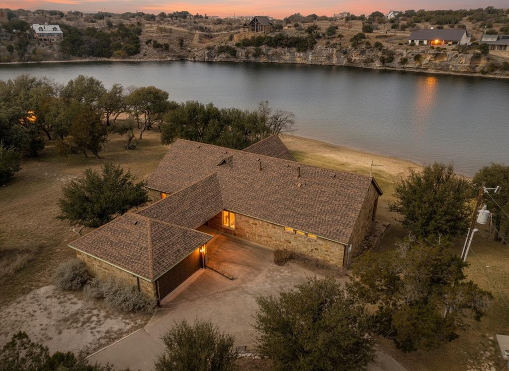 See to believe!  Enjoy this gently sloping lawn onto a rare sandy beach in smooth no-wake water, allowing you to beach your boat and watercraft just a few steps directly in front your home. From there, & from the elevated covered patio that runs the full length of the home, you have amazing views of famed Hells Gate & the surrounding bluffs, with front row seats to the spectacular Fourth of July fireworks, iconic Hell’s Gate cliff diving, & serene glassy deep water.  Built in 2012 to maximize the water features and efficiently use the interior space, the one-level ranch-style residence offers an open great room, dining, & kitchen with an architecturally compelling vaulted ceiling, anchored by a wall of windows across the length of the home, bringing the lake indoors year-round. Double glass entry doors, beautiful cabinetry, 8’ tall doors, rich wood floors, 7” baseboards & 10' high ceilings throughout the home show the home was built to a higher standard. The oversized primary suite features full lake views & the junior master bedroom offers a private en-suite bath; and generously sized bedrooms 3 & 4 share a third full bath. A spacious laundry and pantry room includes a 10’ long countertop, washer and dryer, and a second refrigerator, ideal for extra food & supplies for large gatherings. This resort-style property is accessed through an electronic gate at the road and features a concrete circular driveway winding through secluding trees. The garage connects to the home via a porte-cochère, which provides additional covered parking. The outdoor living area is fully equipped with a built-in grill, speakers, and television—perfect for entertaining and watching your family and guests’ activities across the lawn and in the water.  Keep your boat and waverunners a short ride away at Bluff Creek Marina (let them handle the hassles and expense of boat dock ownership!). All furnishings and water toys are available for purchase, offering a true turnkey lakefront lifestyle.