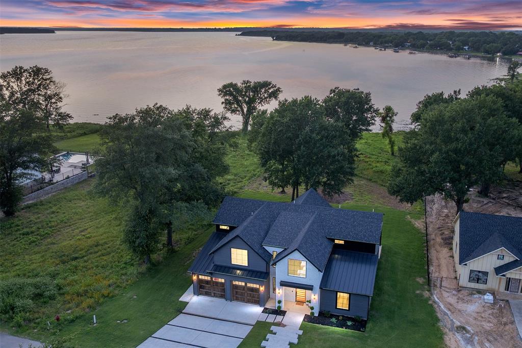 This modern farmhouse mini mansion on the water is truly a remarkable find, set on over half an acre with breathtaking waterfront views. When you step inside, you’re immediately captivated by a wall of windows that frame stunning views of the lake. The home boasts engineered hardwood floors throughout, quartz countertops, and beautifully tiled bathrooms. The heart of this home is the kitchen, designed for both chef enthusiasts and casual cooks alike. It features plenty of space to move around, custom cabinets that include lit display cases at the top. Gorgeous bubble chandeliers hang gracefully over the spacious kitchen island and the dining table. A wall of windows off the dining area allows for uninterrupted lake views. The cutting-edge appliance package includes black stainless steel by Z Line, with a standout oven from the luxury brand Thor, known for its association with Gordon Ramsay. This oven has all the bells and whistles, making it a dream for any culinary enthusiast. The open floor plan seamlessly integrates these areas. The primary suite is conveniently located on the first floor, featuring a luxurious bathroom that has a grand wet room, reminiscent of upscale residences. As you ascend the staircase, adorned with a grand chandelier, you’ll find an overlook that provides a stunning view of the great room with up to 17' ceilings. The second floor offers a fantastic space for guests or family members, complete with a game room and TV area.   A large concrete pad invites gatherings around a fire pit, creating a perfect spot for entertaining friends and family. This gated community also provides private amenities, including an infinity-edge swimming pool, boat ramp, and a gym, making this home an ideal location for a luxurious lifestyle filled with recreation and relaxation. This home, built by Coastal Plains Custom Estates, showcases the most trendy styles, finishes.
