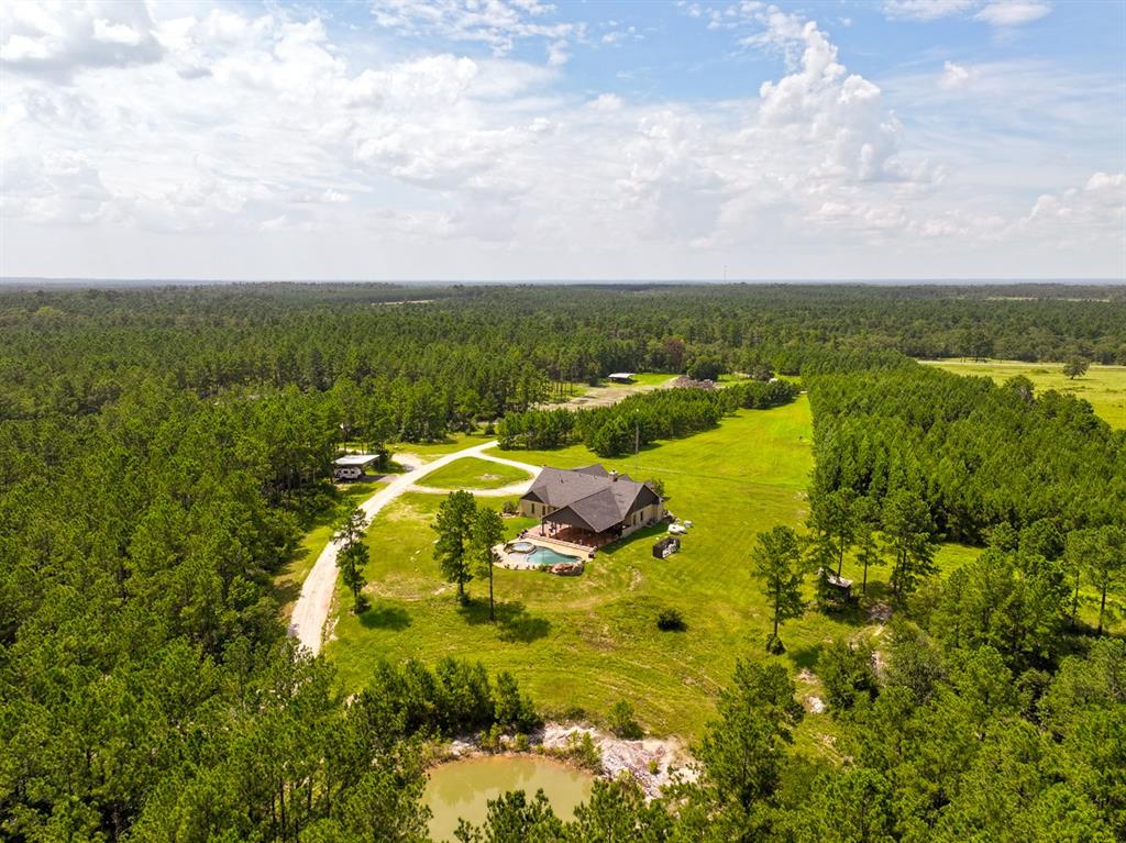 Welcome to 1682 FM 980 in Huntsville, TX a remarkable 60-acre luxury ranch retreat offering the perfect mix of elegance, functionality, and outdoor adventure. Nestled behind a gated entrance and bordered by state-owned land for added privacy, this unrestricted property features rolling terrain, mature pines, scenic trails, natural rock formations, and a seasonal creek. At its heart is a 3,108 ft custom stone home with 3 bedrooms, 3.5 baths, a formal dining room, spacious living area with wood-burning fireplace, and a bonus room ideal as a 4th bedroom or office. The primary suite includes a large walk-in closet, soaking tub, and walk-in shower. High speed fiber internet and underground electricity make it ideal for remote work. A two-car carport, 22 kW propane generator, and two storage tanks add convenience and reliability. Outdoor features include an Austin stone in ground pool with waterfall, hot tub, and a covered patio with outdoor kitchen. A nearby pond and a second private lake stocked with catfish, perch, and minnows add to the experience. A smokehouse and event pavilion make entertaining easy. The 1,600 ft metal shop includes concrete floors, 14' x 14' drive through doors, a 25' x 40' awning, dual 25' x 65' lean-tos, a storage room with water or drain hookups, loft, and separate restroom. Additional improvements include a 30' x 40' equipment awning with 30' x 30' lean-to and a 25' x 25' RV or camper cover with 12’ eave height. Wildlife is abundant deer, hogs, and bobcats roam the land, with hunting lanes, feeders, and blinds in place. The property is serviced by community water and has an ag exemption to help reduce taxes. Whether you're seeking a full-time home, event venue, business base, or weekend retreat, this one-of-a-kind property delivers unmatched versatility, privacy, and value just minutes from Huntsville and close to Houston.