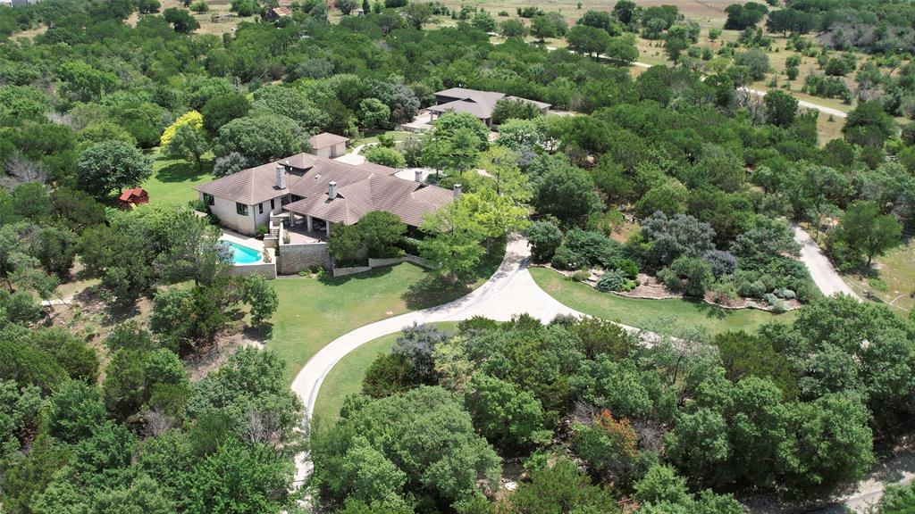 Set on 8.77± acres along one of Aledo's most coveted and private streets, this exceptional single-level estate represents a rare blend of timeless architectural design and refined modern luxury. Thoughtfully positioned to capture natural light, the home features three wood-burning fireplaces, a concrete tile roof, and recently installed energy-efficient windows that combine durability with elevated style. The private primary suite serves as a true retreat, complete with its own fireplace, dedicated study, and a spa-inspired bath designed for both function and indulgence. Interior finishes include a curated combination of hardwood and carpeted flooring, balancing warmth and design continuity throughout. Outdoor living is equally distinguished, anchored by a resort-style pool and cabana, multiple covered patios, and intimate seating areas ideal for quiet enjoyment or large-scale entertaining. A dedicated pool house with full bathroom and ample storage further enhances the experience. A separate 2,700± sq ft guest house provides exceptional flexibility for multi-generational living or hosting, featuring a full kitchen, laundry, climate-controlled wine room, full bath, and attached 4-car carport. Additional highlights include an upgraded water system supported by both Trinity and Paluxy aquifer wells and generous storage throughout the estate. Located within the highly acclaimed Aledo Independent School District, this offering combines privacy, architectural integrity, and elevated lifestyle amenities in one of Parker County's most desirable settings—a truly distinctive opportunity for the discerning buyer.