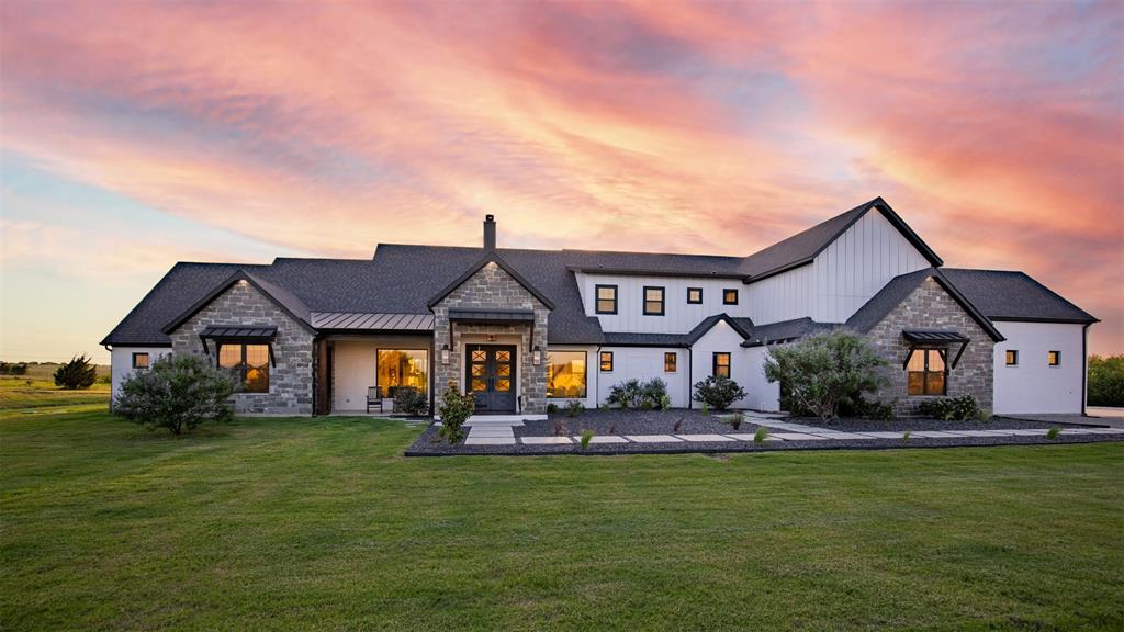 Set within the breathtaking landscape of the coveted Hills of Lone Star community and positioned along the edge of Collin and Grayson Counties, this extraordinary Contemporary Texas Modern Farmhouse delivers a rare combination of refined design, privacy, and expansive Texas views. Situated on 3.237 AC, the property offers a true retreat lifestyle while remaining within reach of everyday conveniences. A striking arrival begins with a custom pathway framed in dramatic black obsidian leading to handcrafted Entrada 8-foot double iron doors. Inside, thoughtful architecture and artisan details create unforgettable spaces. The soaring open-concept living areas are anchored by a dramatic floor-to-ceiling wood-burning fireplace crafted from Silvermist chopped stone and finished with custom live-edge mantels. Custom lighting throughout serves as functional artwork. The chef’s kitchen features stunning Shadow Storm Brazilian single slab leathered marble island, extensive cabinetry, abundant storage, Black Diamond commercial range with six 12x12 grills and one 24x21 inch griddle, and a fully cabinet-lined walk-in pantry with fridge and ice maker. The private primary wing is a destination of its own, offering a dedicated office, in-room coffee bar, direct laundry access to walk-in-closet, and a spa-inspired bath with radiant heated floors, 2-person jetted tub and private walk-in shower. The home also includes a secondary suite downstairs with heated bathroom floors, walk-in closets throughout, soundproof media room, upstairs and downstairs laundry rooms, finished attic flex space, spray foam insulation, tankless water heating, and 20-zone sprinkler system. Car enthusiasts and adventure seekers will appreciate the exceptional open style garage that can accommodate up to 8 cars and features an extra-tall bay ideal for RV, boat, or specialty vehicle storage. Property is bordered by 500 AC family owned property and Trinity River Valley. One-of-a-kind Texas estate!