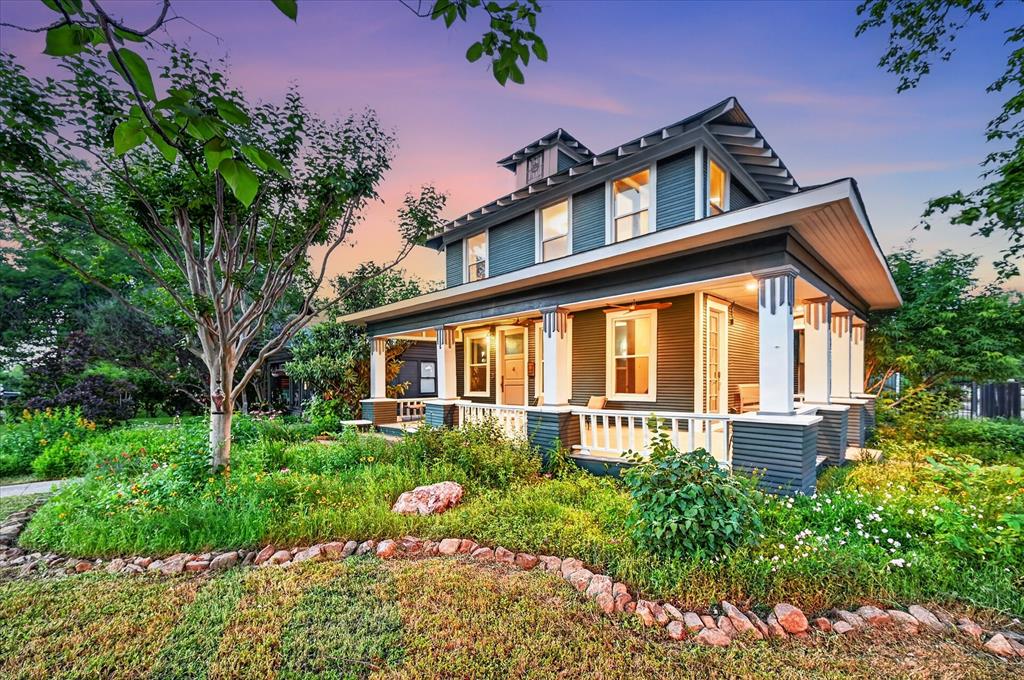 Charming 1918 historic home with over a century of character, blending timeless architecture with thoughtful modern updates, located just blocks from the Bishop Arts District and Kidd Springs Park. Showcasing where early 1900s charm meets Art Deco influence, the home features moody tones, vintage hardware, designer lighting, and curated details that create a soulful, one-of-a-kind atmosphere. Oversized living spaces begin with a moody listening parlor, flowing into a flexible dining area, library or flex space that can easily function as a guest room with access to a full bath. The open-concept kitchen and living area offer a warm, inviting layout ideal for entertaining. Rich in history, the home highlights preserved early 1900s craftsmanship—from original doors and molding to thoughtfully maintained finishes—seamlessly paired with modern updates. Upstairs features a large living area that can serve as an extension of the primary suite. Down the hall, guest quarters, full bath, bedroom, and a light-filled sunroom—ideal for a yoga or workout space. Picture sitting back on wrap around front porch and taking in the lush, established landscaping. Detached garage with loft and rear space offers potential for a studio, guest quarters, or creative retreat.