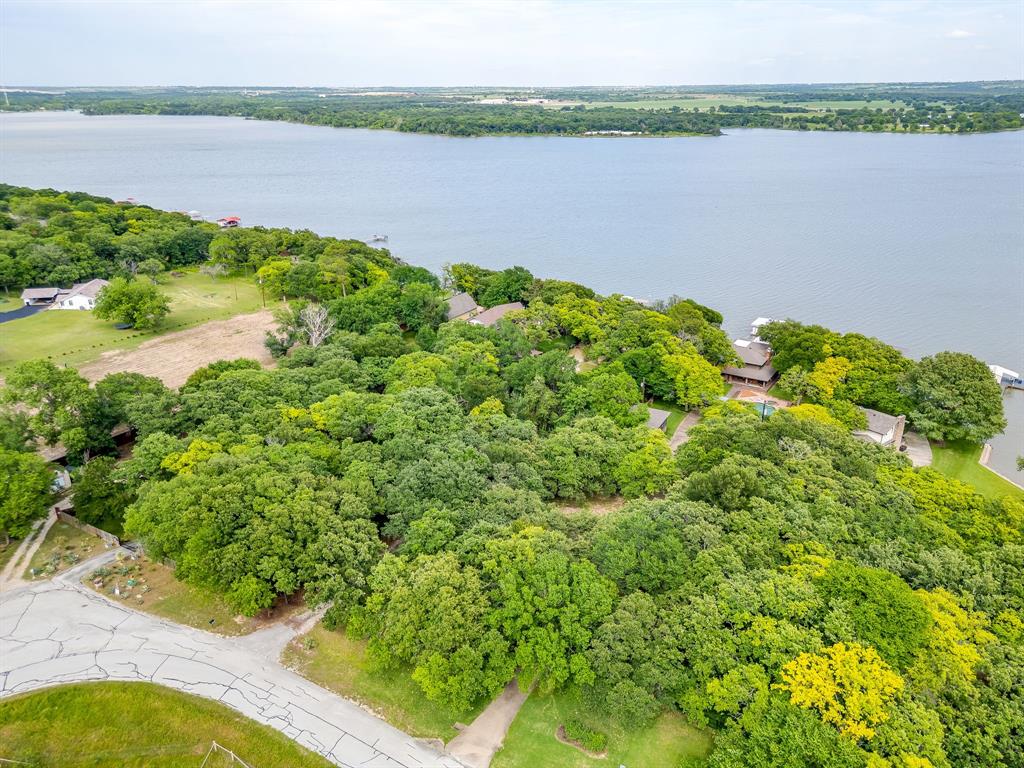 Welcome to a rare waterfront opportunity on 1.22 acres along the open waters of Eagle Mountain Lake. Tucked behind a beautifully tree lined gated entrance, this private and fenced property offers a peaceful retreat surrounded by towering mature trees, expansive lake views, and the serenity of nature. The setting is truly special, with a long gated drive creating a sense of arrival while providing both privacy and seclusion.  Positioned on deep open water, the property captures breathtaking panoramic views and offers direct access to the lake for boating, fishing, and recreation. Multiple outdoor spaces allow you to enjoy the scenery, shade, and tranquil atmosphere created by the abundance of mature trees surrounding the property. Whether you are looking for a weekend escape, future dream home site, or a full time waterfront lifestyle, the land itself is the true highlight of this property.  The property includes a main house with two bedrooms, two baths, multiple living areas, and lake facing windows that maximize the waterfront views. A separate guest house with kitchen and full bath provides additional flexibility for guests, rental potential, or multigenerational living. Storage buildings and additional improvements offer functionality and convenience while leaving ample room to personalize the property to your vision.  With gated access, fencing, mature landscaping, open water frontage, and endless potential, this Eagle Mountain Lake property presents a unique opportunity to own a private slice of waterfront paradise in one of the lake’s most desirable areas.  Call for your private showing today!