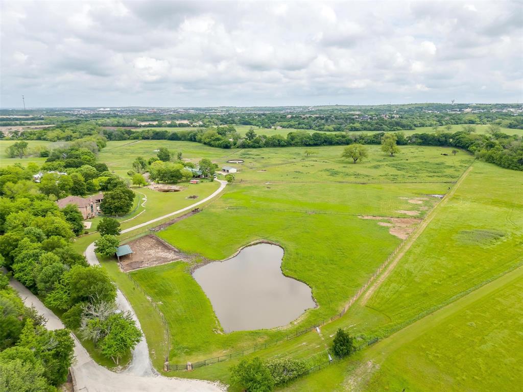 Just over 30 acres and more than 5,000 square feet of luxurious living space located just outside downtown Aledo! Experience the epitome of grandeur at this elegant residence, with soaring ceilings, large picture windows and multiple living spaces, creating a sense of spacious elegance and comfort. The beautiful manicured and cross fenced land spanning over 30 acres is a true haven for anyone hoping to raise or train horses. The property boasts a horse barn with 11 stalls, serene paddocks, and even a stone bridge. There is also a guest home on the property, which is over 2,000 square feet. The back portion of the property boarders the winding Trinity, providing privacy and serenity. Enjoy leisurely afternoons by the pool, surrounded by the breathtaking scenery of this private estate. This is an exceptional opportunity to embrace the country lifestyle, as well as the enjoyment of grandeur and sophistication this wonderful home provides all just minutes from the heart of Aledo, TX.