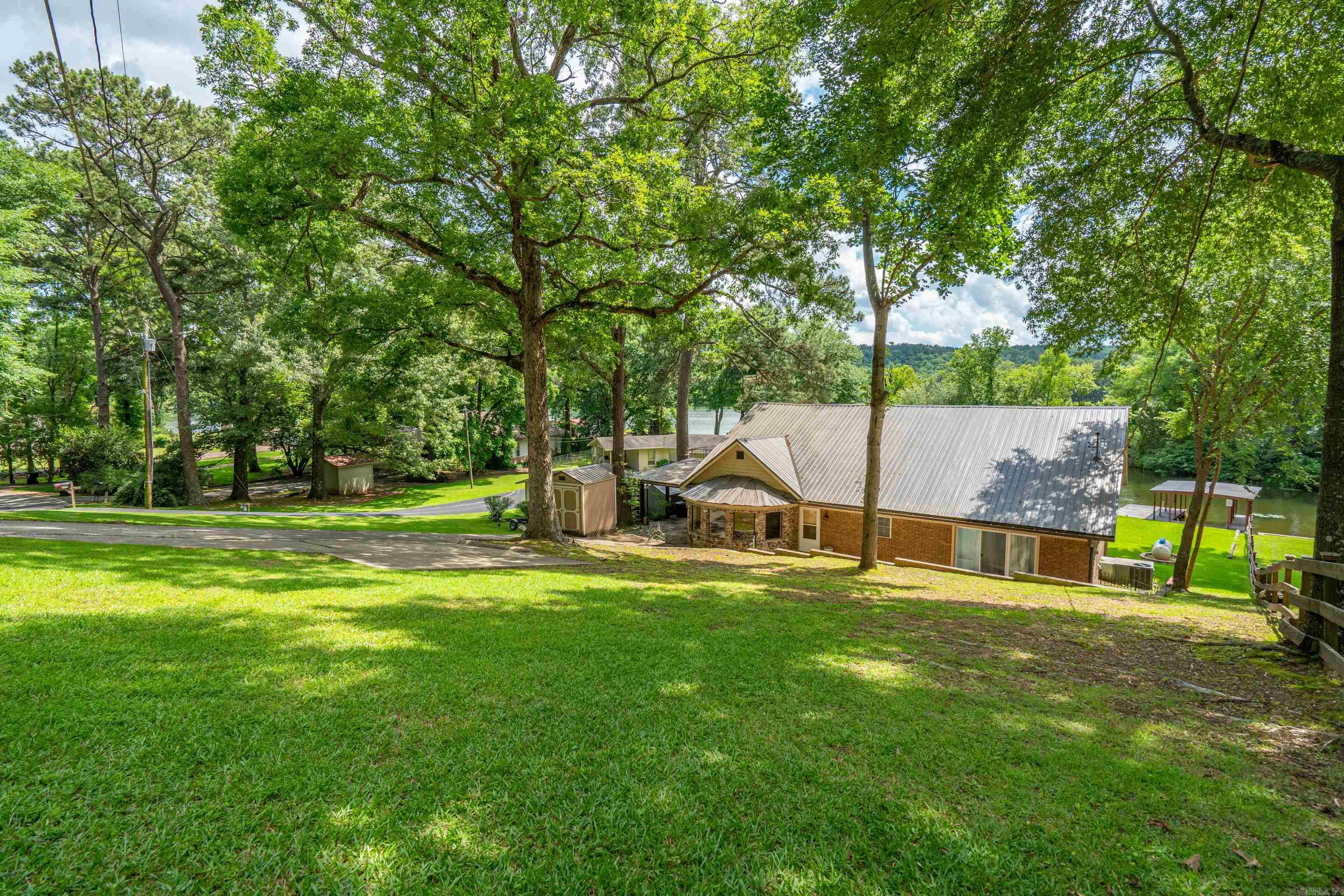 Descending the driveway to the carport, outdoor living is enhanced with a back patio along with a tucked away back porch and a level lot that leads gently to the water and a covered one-slip boat dock with an attached swim dock. This retreat is in plain sight of the main channel with great views while remaining protected from heavy wave action. A partially fenced backyard adds a little privacy AND a safe haven for your fur babies! From the carport you can reach the upper deck that offers massive insight to the area. From this deck you enter the sophisticated main cave. Behind this fun area, there is a large floored attic. The recently updated interior offers TWO master suites and a very large office/game room.  This home blends thoughtful design, comfort and serene lakefront living.  *Pictures made during drawdown. *No flood insurance required.